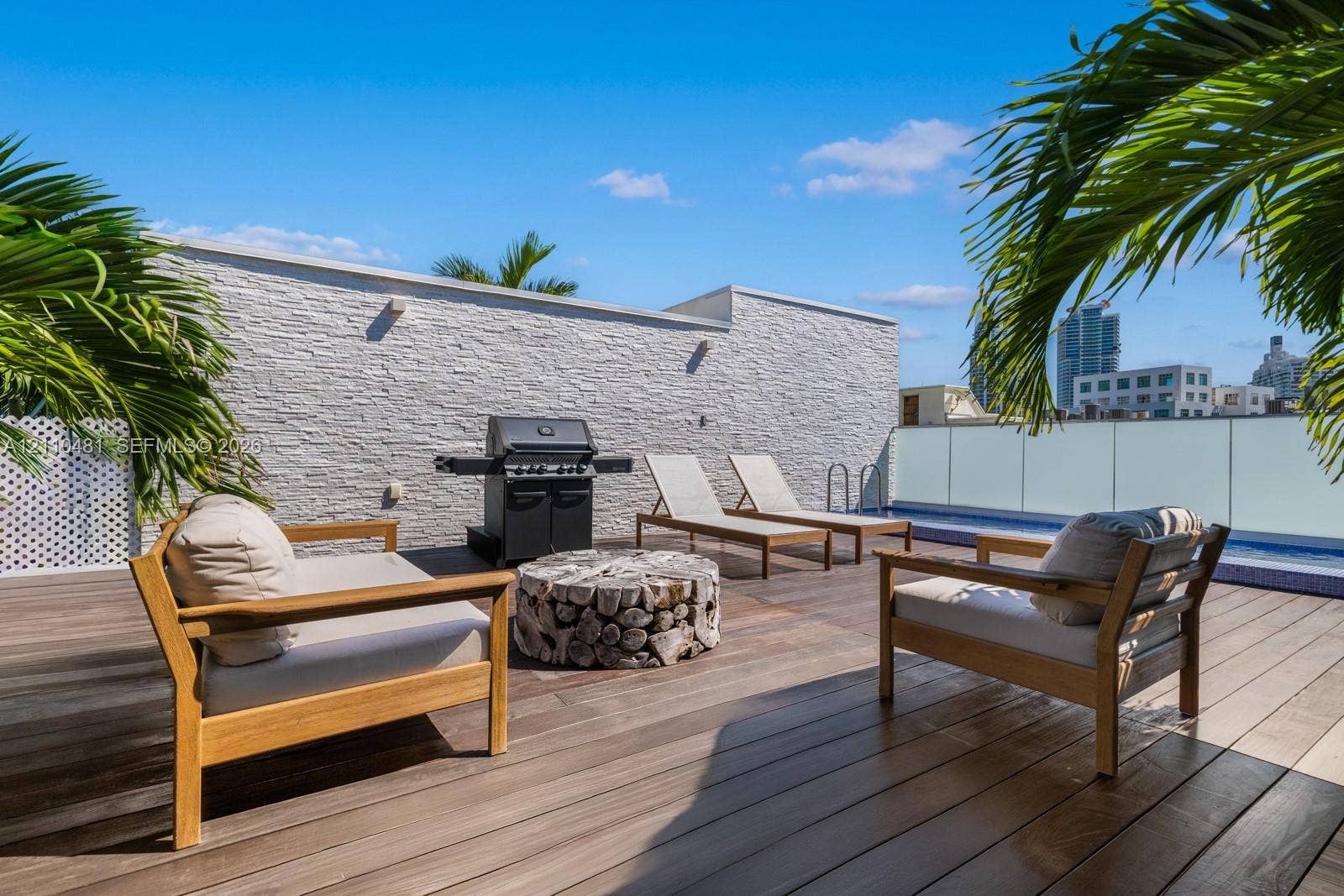 234 Washington Avenue, #D, Miami Beach, FL 33139 Rooftop terrace featuring wood-finish decking, a textured stone accent wall, and a perimeter glass railing system
