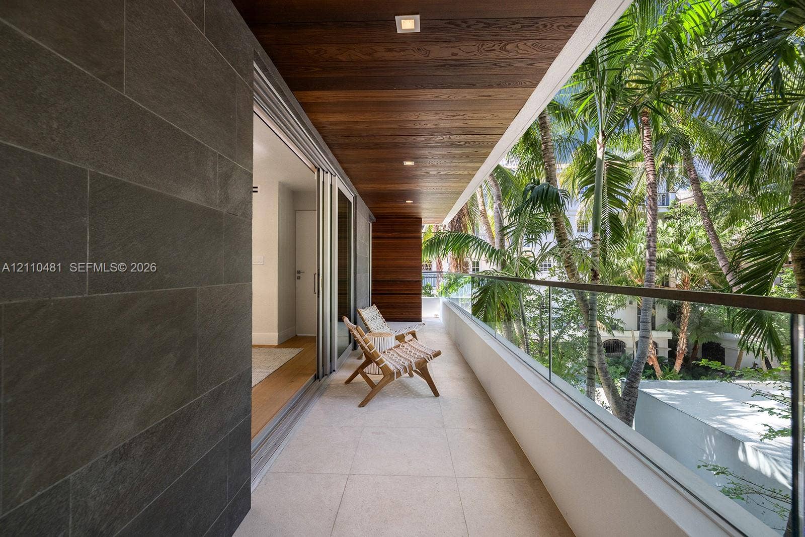 234 Washington Avenue, #D, Miami Beach, FL 33139 Covered balcony featuring large-format stone tile flooring, charcoal-toned stone wall cladding, natural wood-finish ceiling, and a glass panel railing
