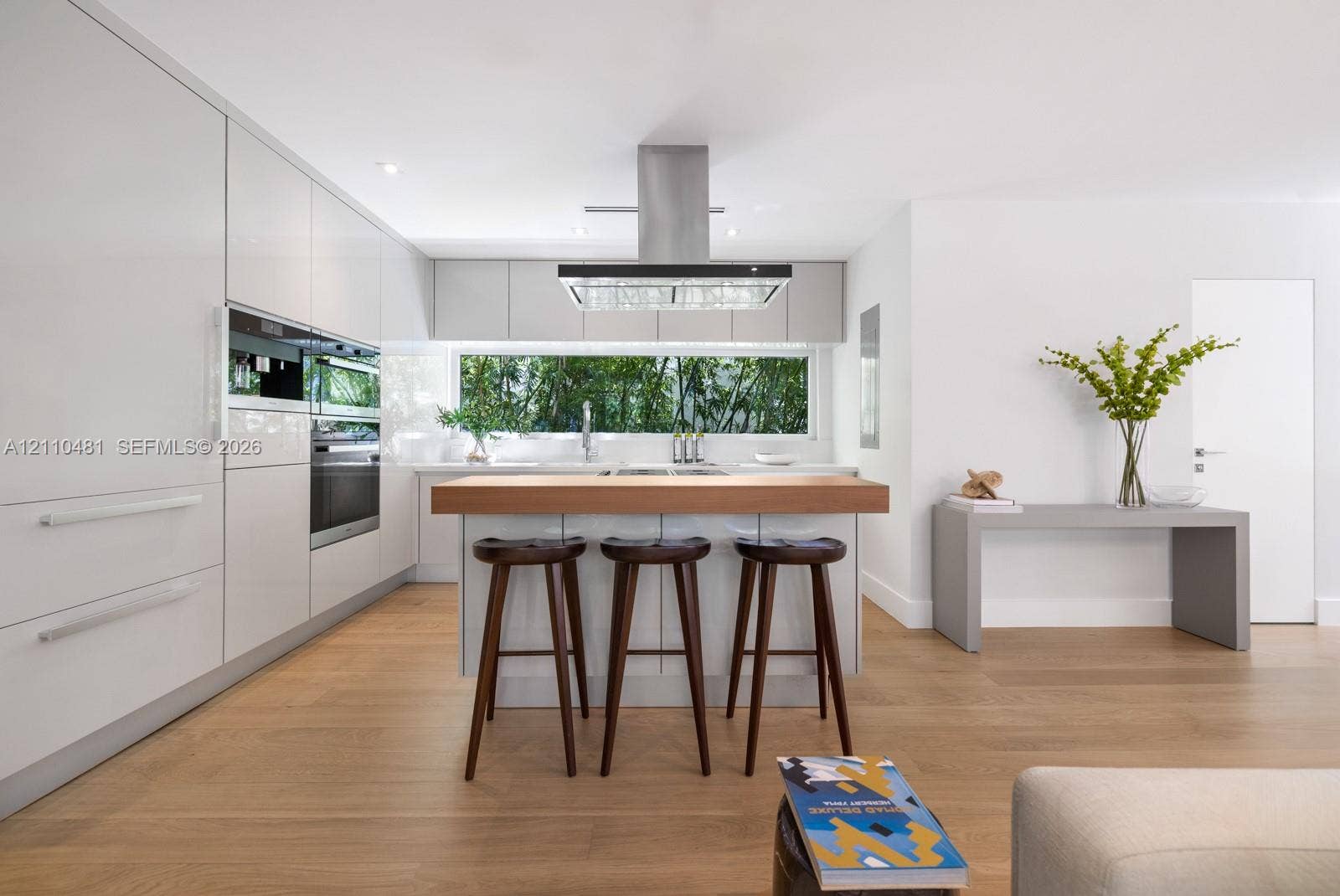 234 Washington Avenue, #D, Miami Beach, FL 33139 Contemporary kitchen featuring flat-panel cabinetry, stainless steel built-in ovens, wood-finish flooring, a center island with a wood countertop, and a stainless steel range hood