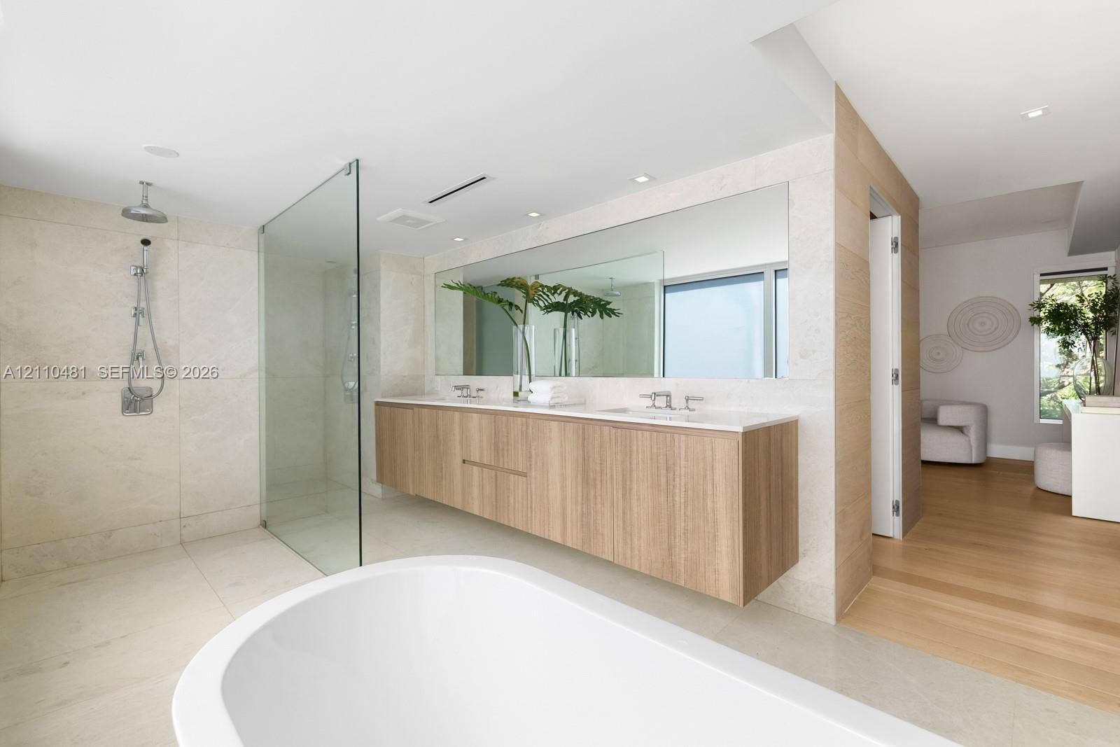 234 Washington Avenue, #D, Miami Beach, FL 33139 Floating wood-finish vanity with dual sinks, stone-tile shower with glass partition, freestanding soaking tub, large wall-to-wall mirror, and recessed lighting
