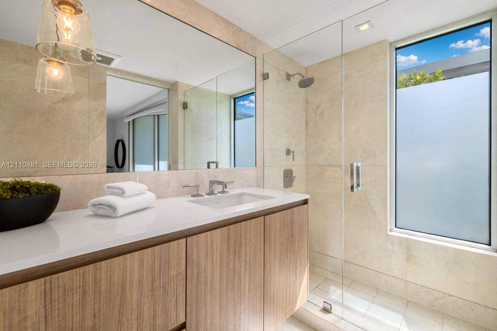 234 Washington Avenue, #D, Miami Beach, FL 33139 Wood-finish floating vanity with white solid surface countertop, undermount sink, glass-enclosed shower with full-height stone-finish wall tile, and large wall-to-wall mirror