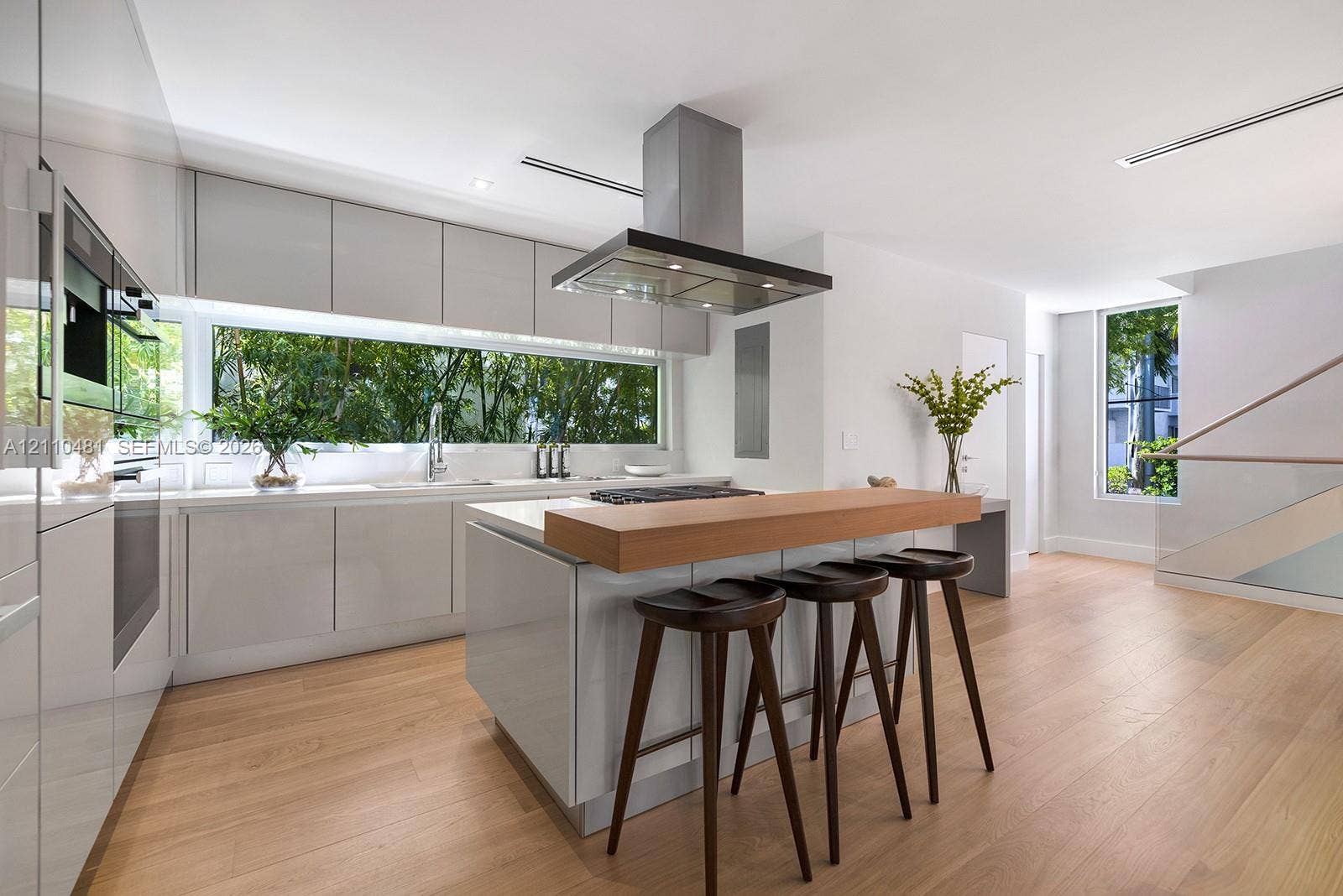 234 Washington Avenue, #D, Miami Beach, FL 33139 Modern kitchen featuring gloss-finish cabinetry, wood-finish flooring, a central island with a wood-tone countertop, a stainless steel range hood, and a horizontal window backsplash