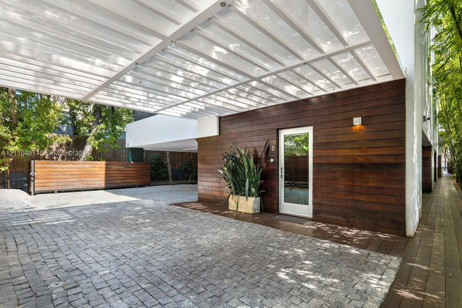 234 Washington Avenue, #D, Miami Beach, FL 33139 Modern exterior featuring horizontal wood siding, a structured metal pergola, stone paver driveway, and an entryway with a glass-paneled door
