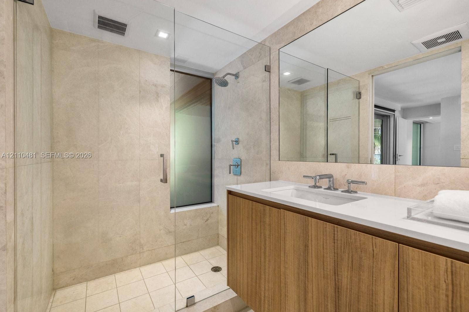 234 Washington Avenue, #D, Miami Beach, FL 33139 Bathroom featuring stone-tile wall finishes, a wood-finish vanity with a white countertop, a frameless glass-enclosed shower, and a large wall-mounted mirror