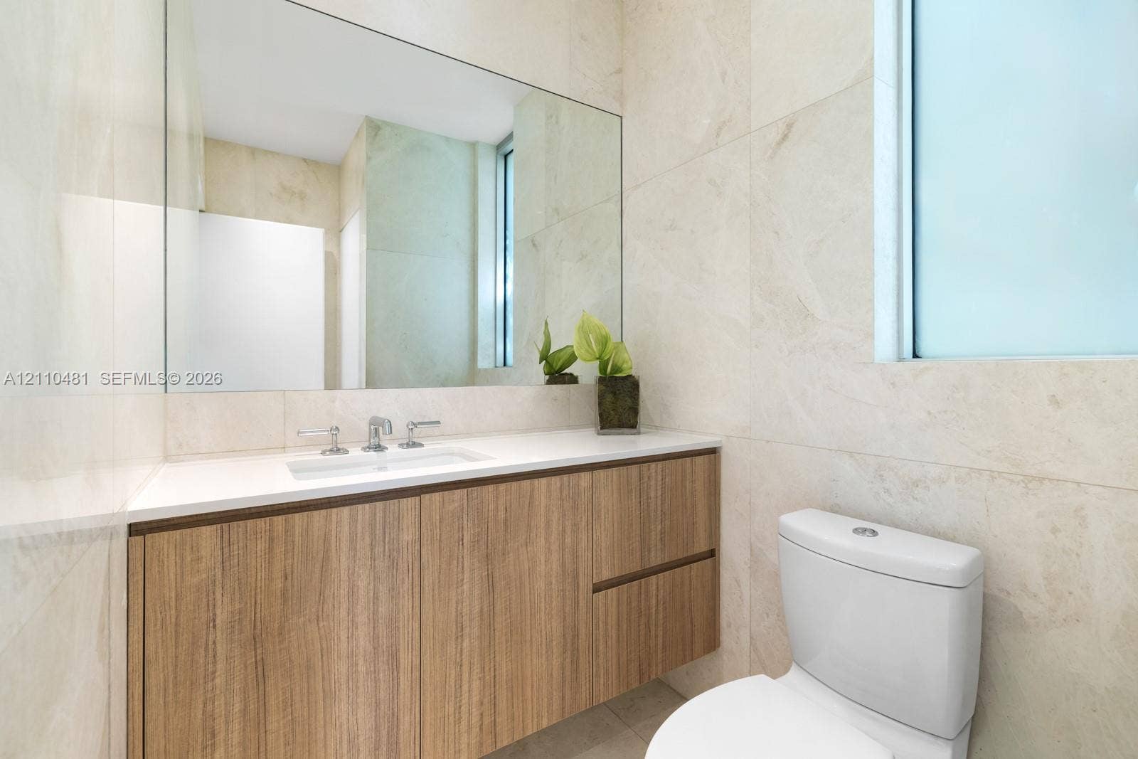 234 Washington Avenue, #D, Miami Beach, FL 33139 Wall-mounted vanity featuring wood-finish cabinetry, white countertop with integrated sink, chrome widespread faucet, large frameless mirror, and floor-to-ceiling neutral tile work