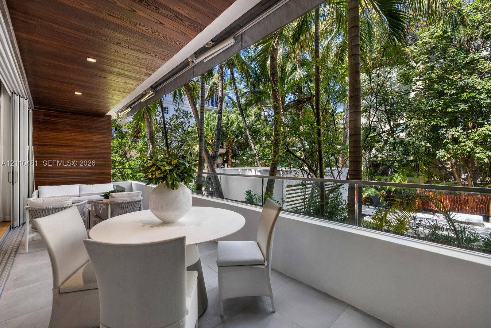 234 Washington Avenue, #D, Miami Beach, FL 33139 Covered balcony featuring wood-paneled ceiling, recessed lighting, tile flooring, and a glass-paneled railing overlooking mature palm trees