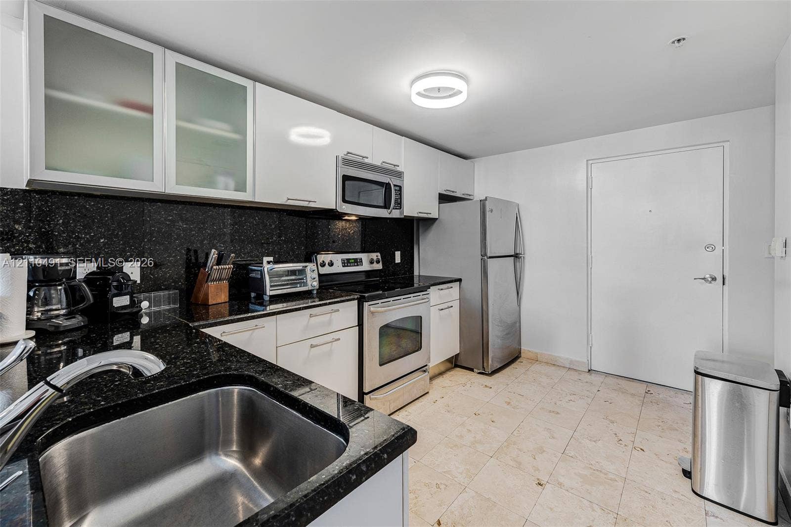 3339 Virginia Street, #136, Miami, Miami, FL 33133 Kitchen featuring white cabinetry with glass-panel upper doors, dark stone countertops, stainless steel appliances, and tile flooring
