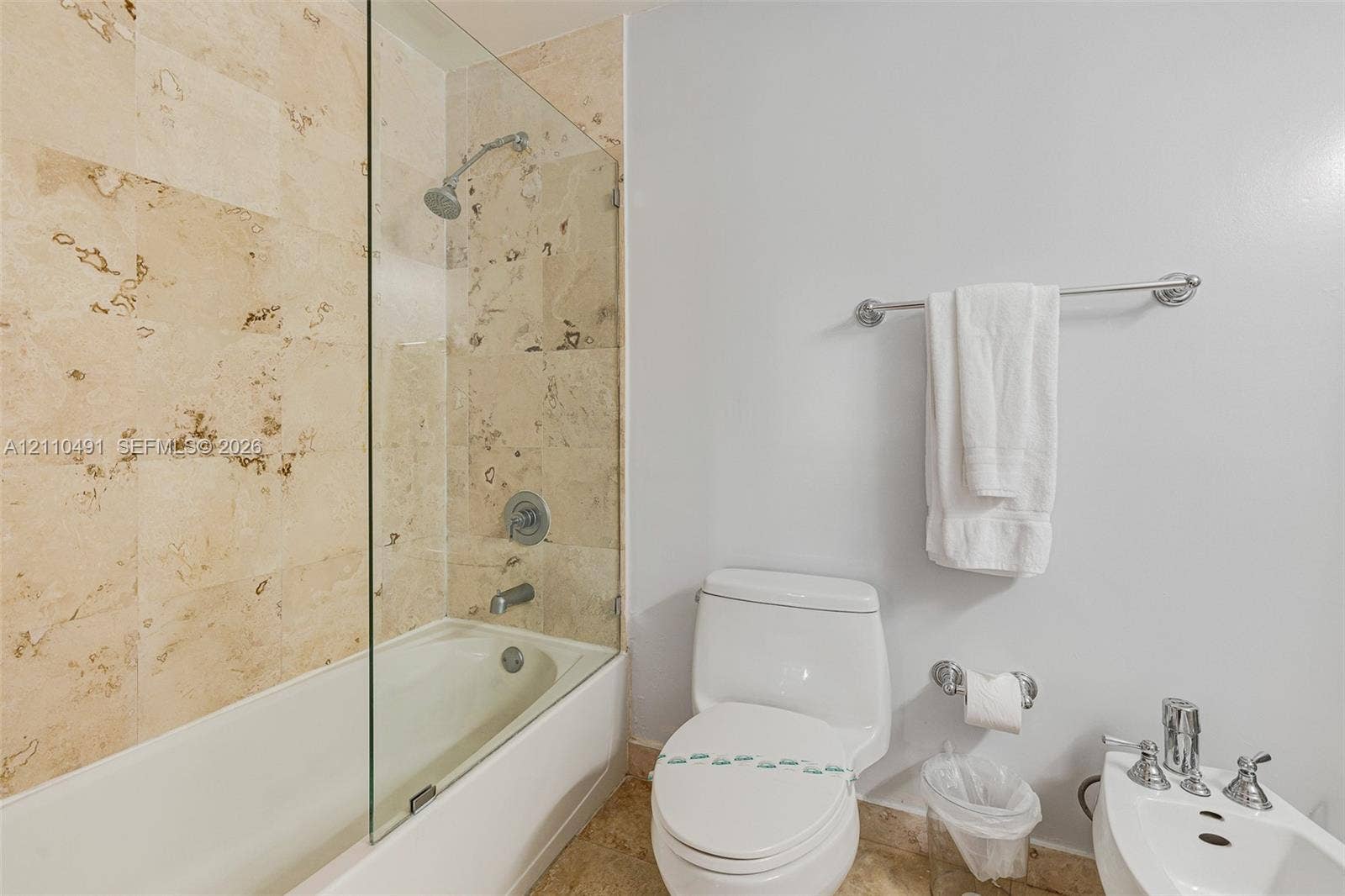 3339 Virginia Street, #136, Miami, Miami, FL 33133 Bathroom featuring stone-tile wall surround, glass shower panel, soaking tub, chrome fixtures, and a white porcelain toilet and bidet