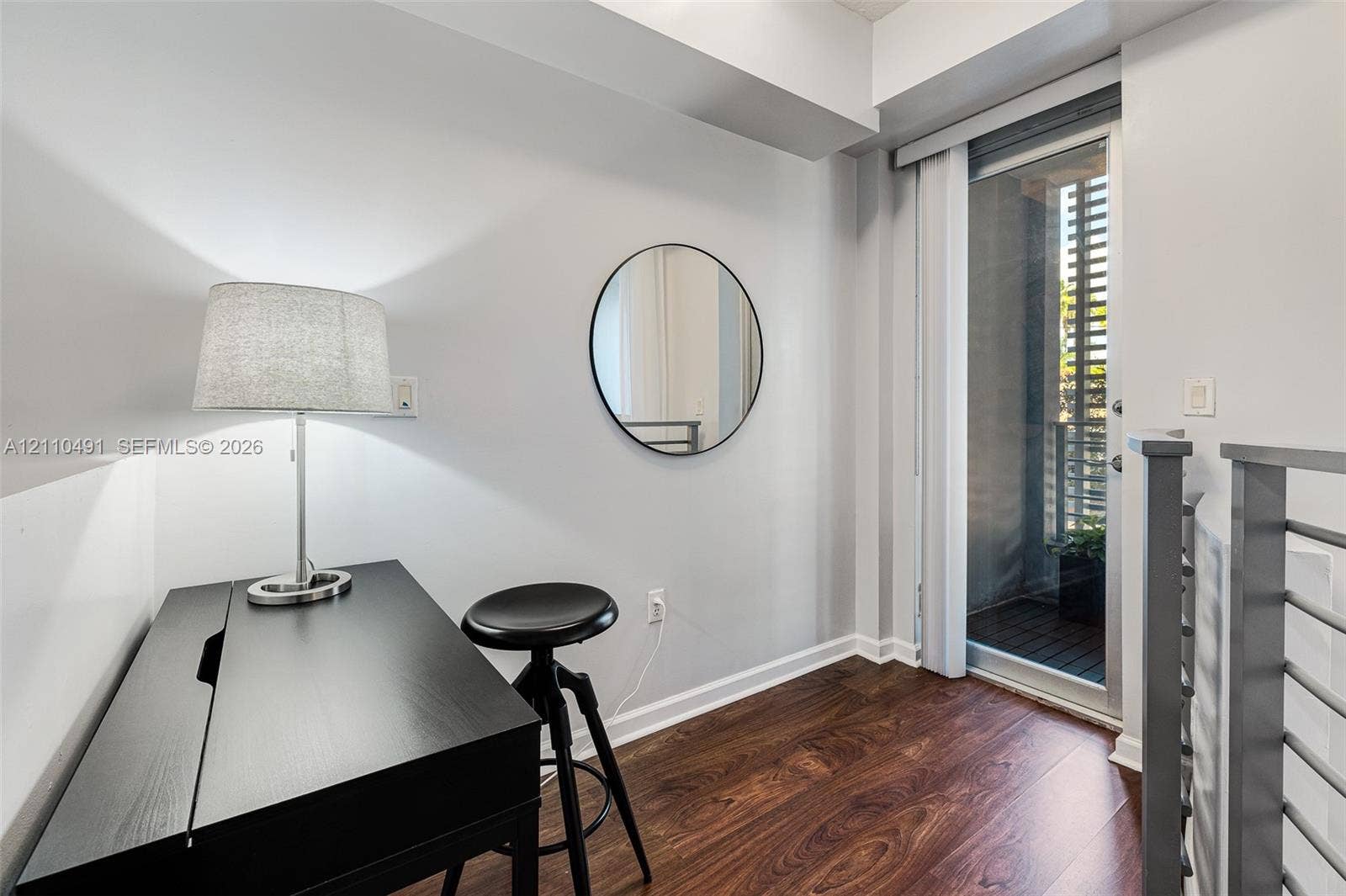 3339 Virginia Street, #136, Miami, Miami, FL 33133 Wood-finish flooring, wall-mounted circular mirror, and glass-paneled door leading to an exterior balcony with metal railing