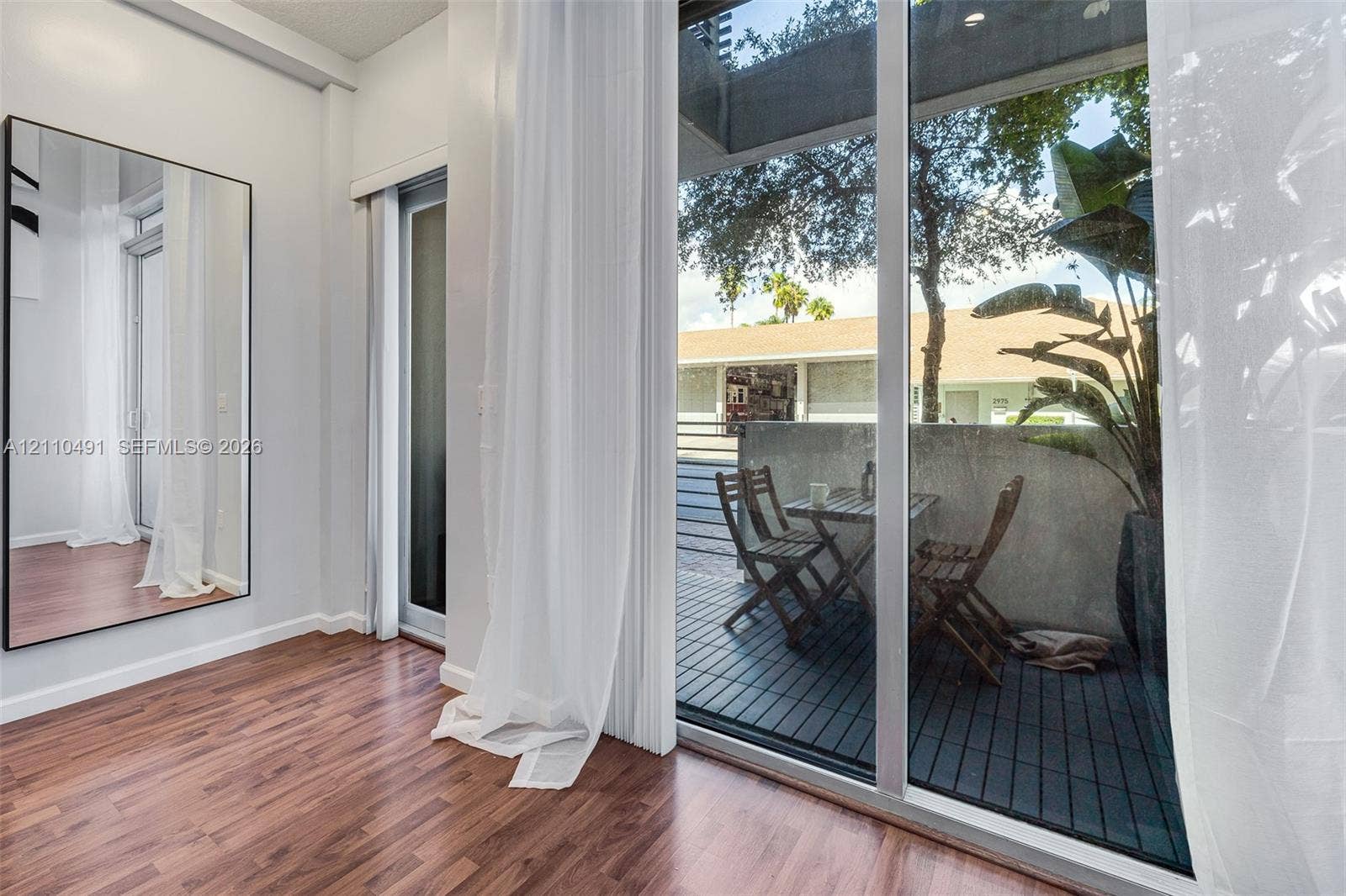 3339 Virginia Street, #136, Miami, Miami, FL 33133 Full-height wall mirror, wood-finish flooring, floor-to-ceiling glass sliding door, and private exterior balcony with slatted decking