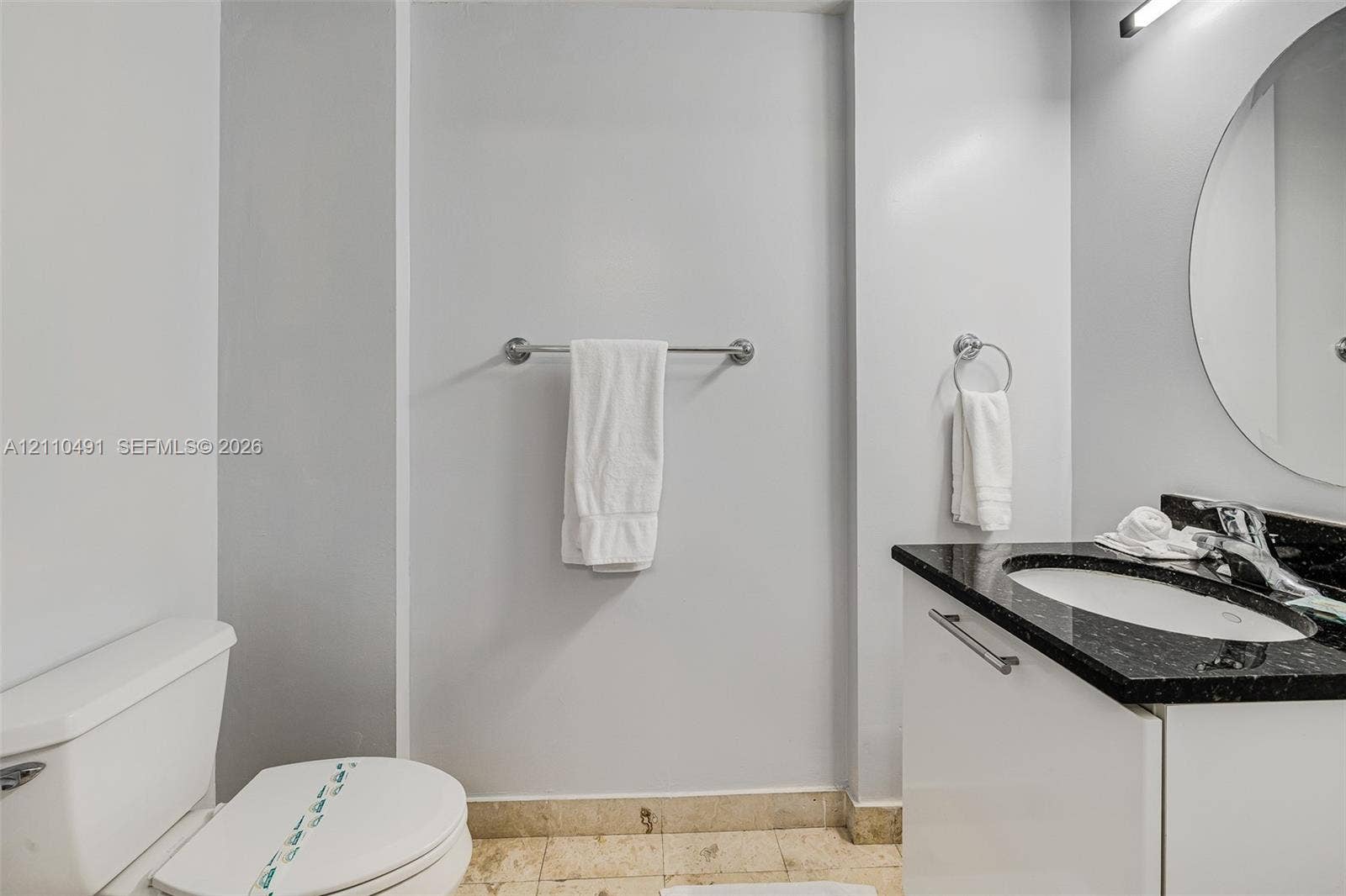 3339 Virginia Street, #136, Miami, Miami, FL 33133 White vanity with integrated basin, dark stone-finish countertop, polished chrome faucet, round wall-mounted mirror, and tile flooring