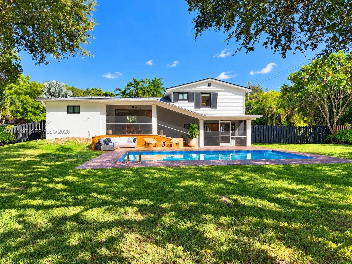 Rear exterior featuring an in-ground swimming pool, brick paver decking, a covered screened-in patio, and a fenced backyard
