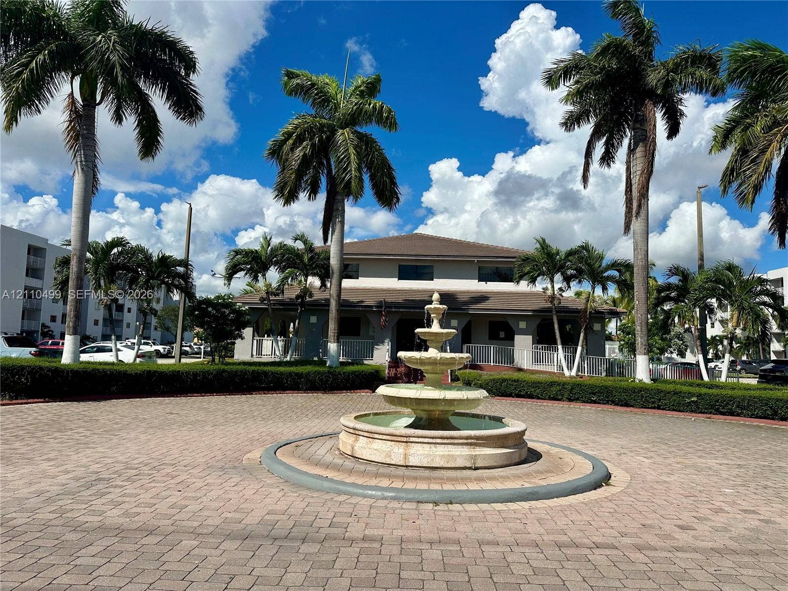 8145 NW 7th Street, #308, Miami, Miami, FL 33126 Circular paver courtyard featuring a multi-tiered stone fountain, mature palm trees, and manicured shrubbery