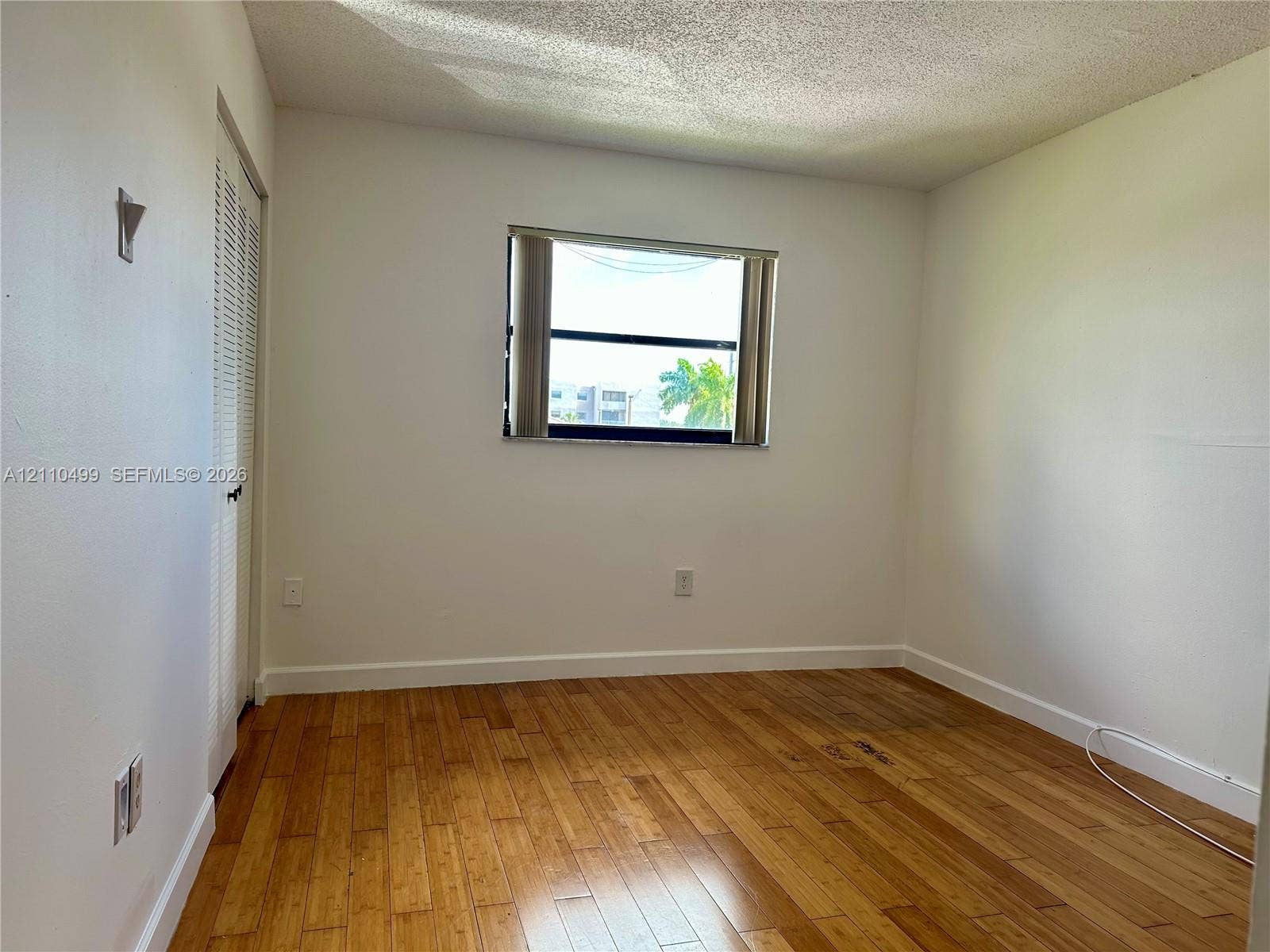 8145 NW 7th Street, #308, Miami, Miami, FL 33126 Room featuring wood-finish flooring, white walls, louvered closet doors, and a central window