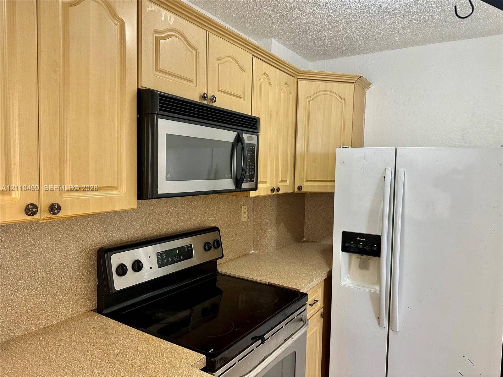 8145 NW 7th Street, #308, Miami, Miami, FL 33126 Kitchen featuring light-finish cabinetry, neutral-toned solid-surface countertops, integrated over-the-range microwave, electric range, and side-by-side refrigerator