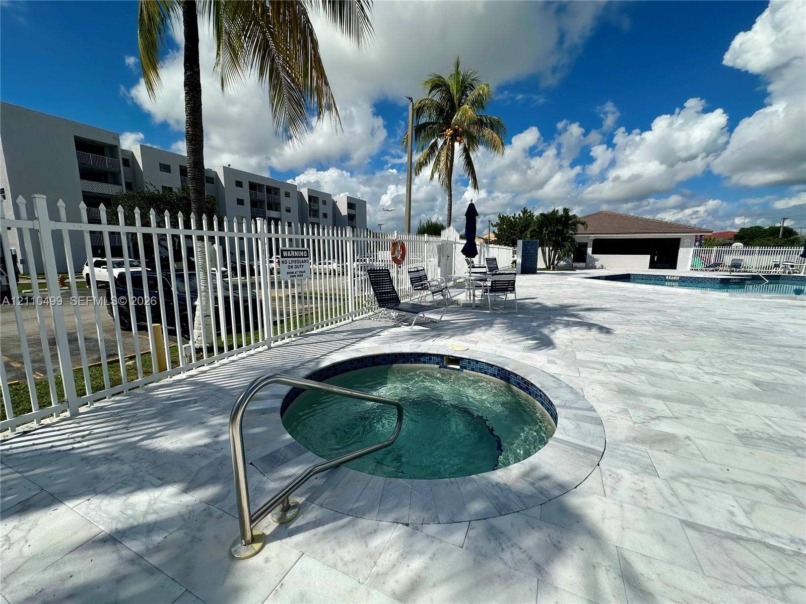 8145 NW 7th Street, #308, Miami, Miami, FL 33126 In-ground spa with a stainless steel handrail, surrounded by light-toned stone decking and enclosed by white metal fencing