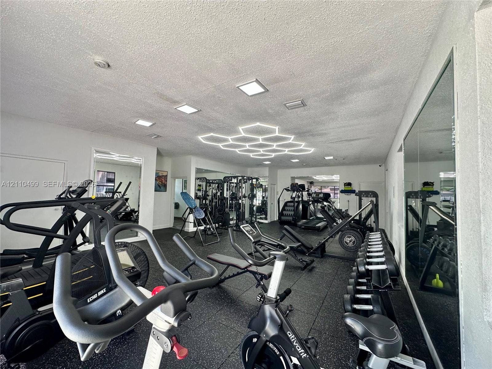 8145 NW 7th Street, #308, Miami, Miami, FL 33126 Interior space featuring durable rubber flooring, large wall-mounted mirrors, recessed lighting, and integrated hexagonal ceiling fixtures