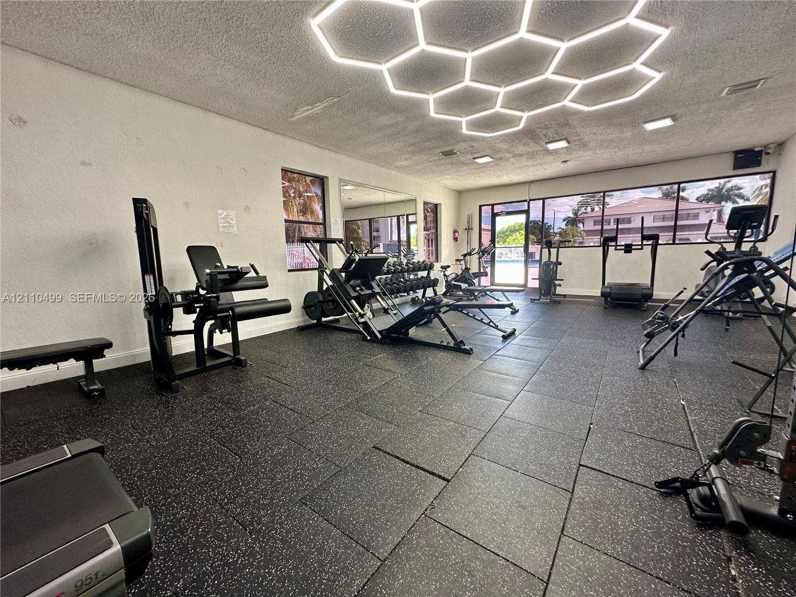 8145 NW 7th Street, #308, Miami, Miami, FL 33126 Fitness room featuring rubberized tile flooring, honeycomb-pattern ceiling lighting, floor-to-ceiling windows, and wall-mounted mirror panels