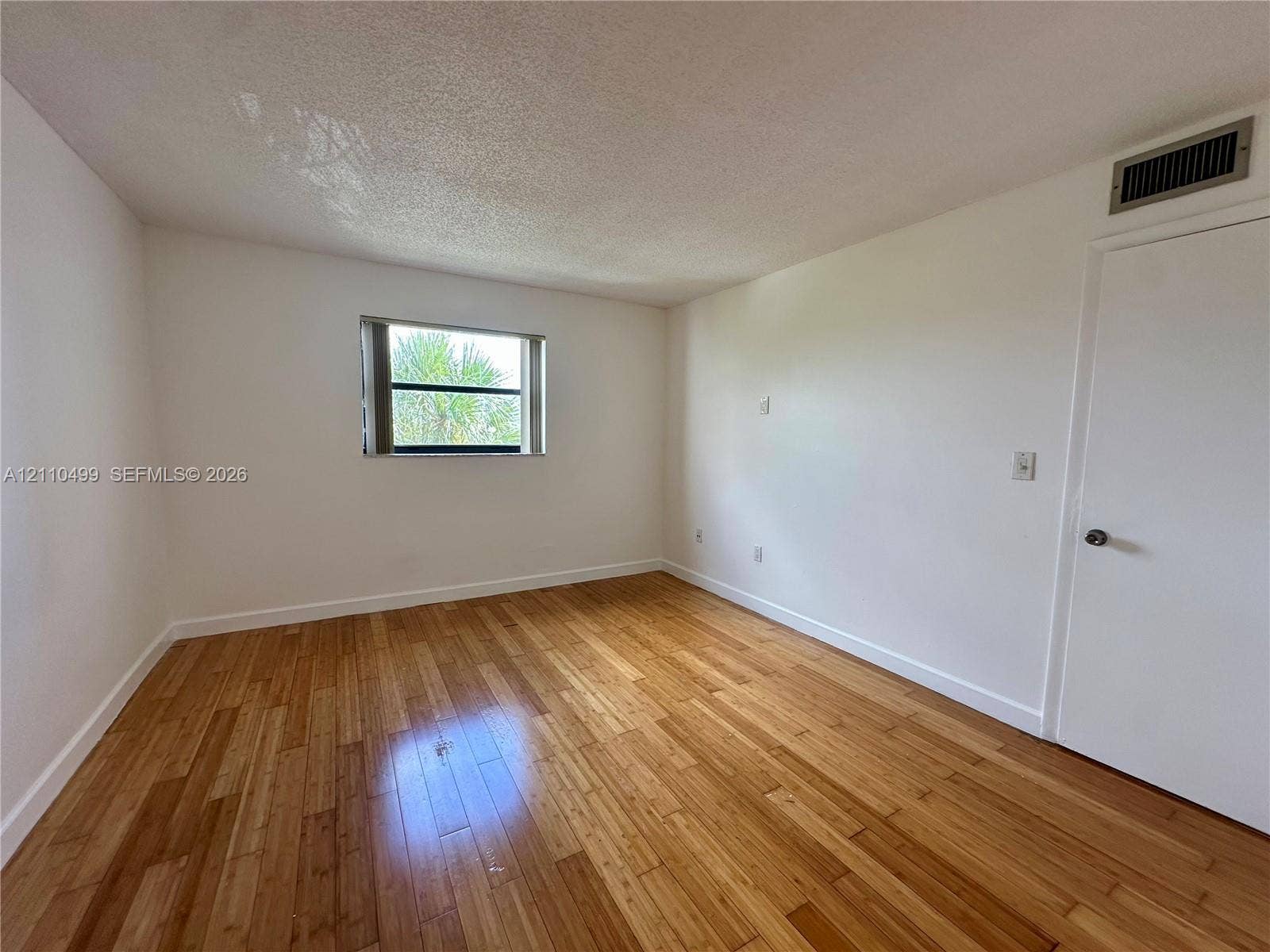 8145 NW 7th Street, #308, Miami, Miami, FL 33126 Room featuring wood-finish flooring, a single-pane window with a horizontal blind, and a solid-core interior door
