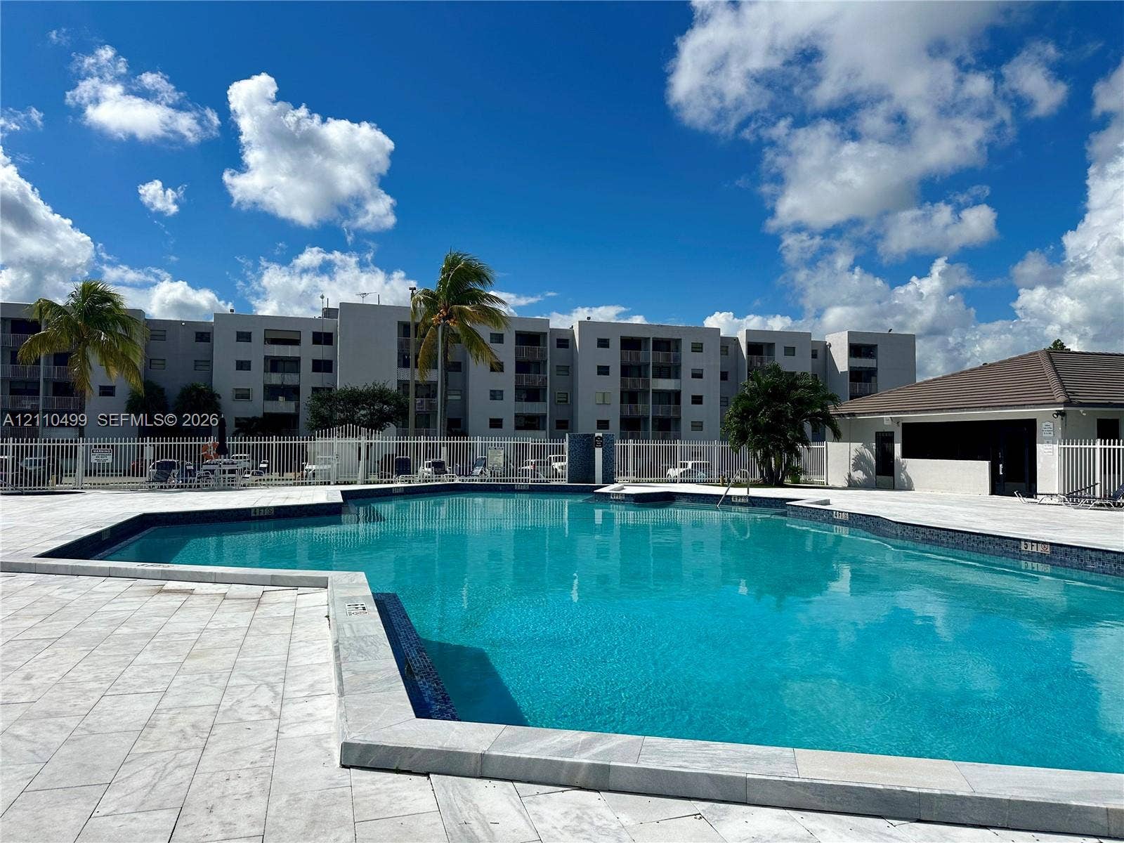 8145 NW 7th Street, #308, Miami, Miami, FL 33126 Swimming pool with tiled decking, perimeter fencing, and surrounding palm trees