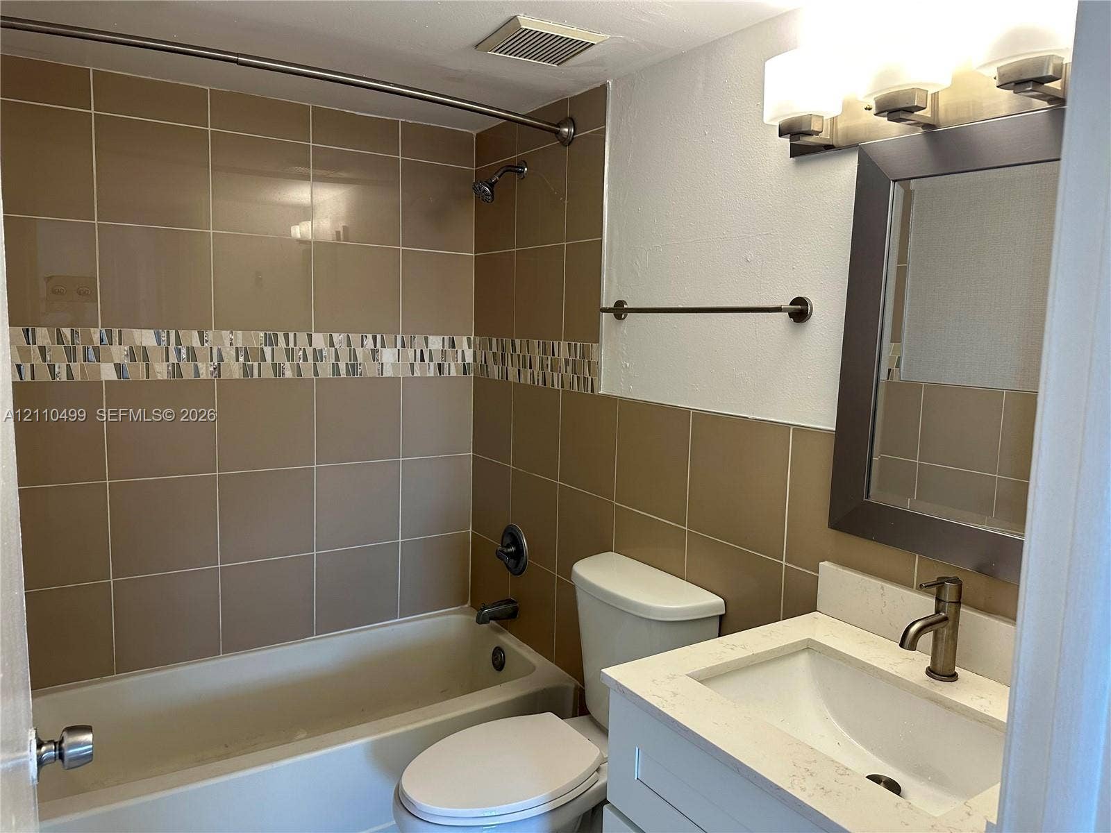 8145 NW 7th Street, #308, Miami, Miami, FL 33126 Bathroom featuring a tub and shower combination with tile surround and decorative accent border, white vanity with stone-finish countertop, undermount sink, and wall-mounted vanity light