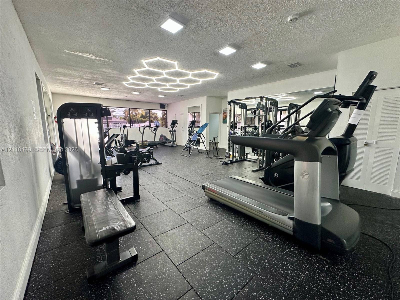 8145 NW 7th Street, #308, Miami, Miami, FL 33126 Fitness center featuring durable rubberized flooring, large-scale wall-mounted mirrors, recessed LED lighting, and a prominent hexagonal ceiling light fixture