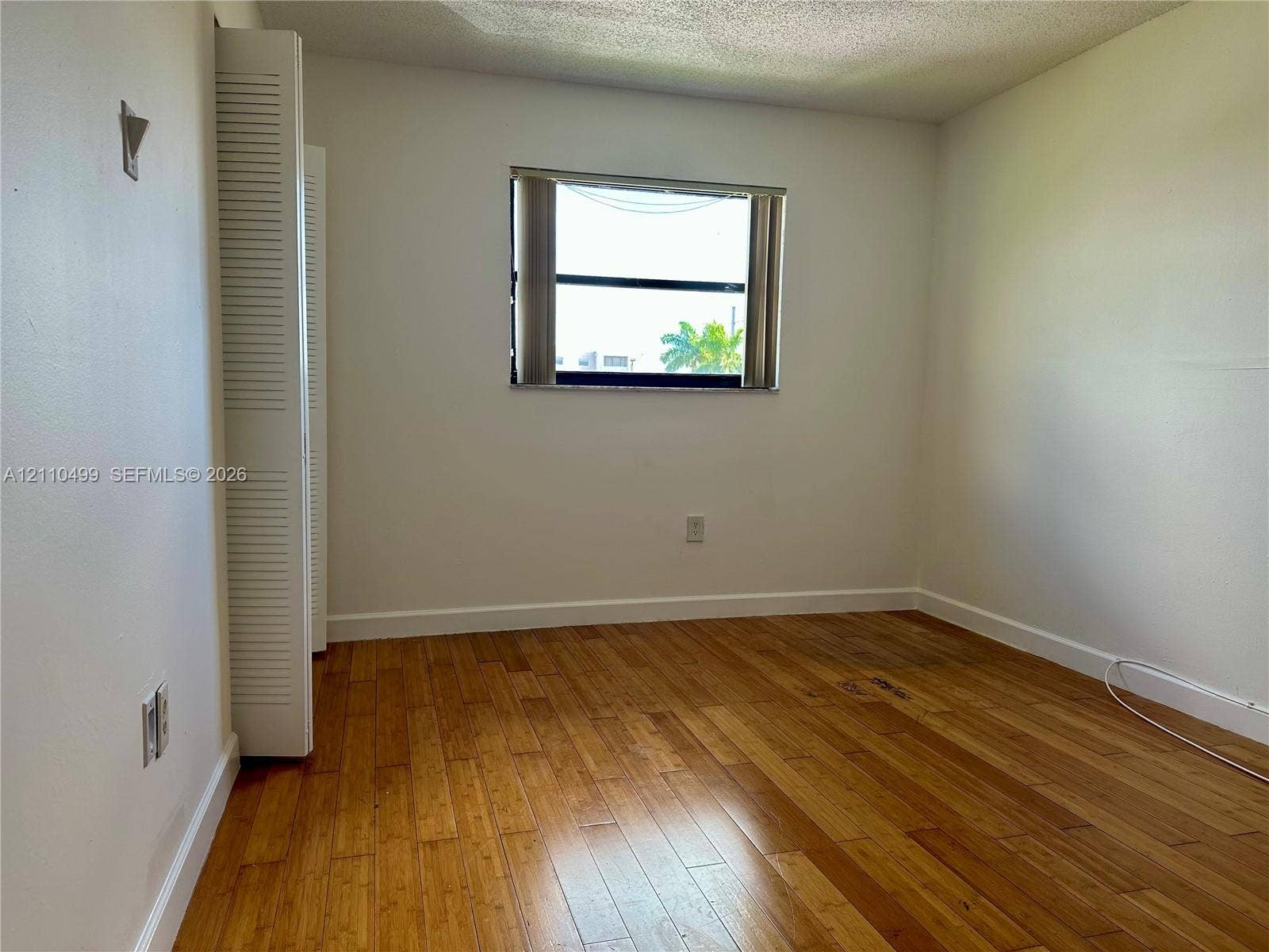 8145 NW 7th Street, #308, Miami, Miami, FL 33126 Interior room featuring wood-finish flooring, a horizontal sliding window, and a built-in closet with louvered doors