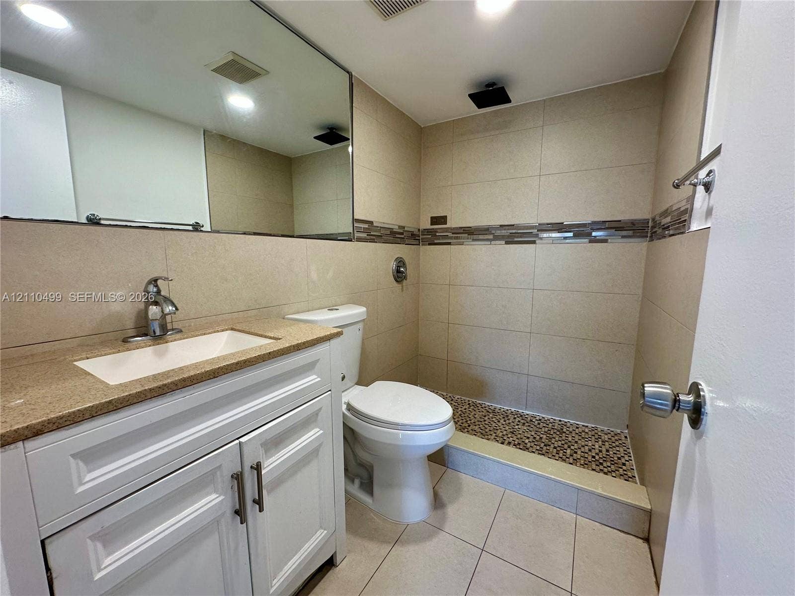 8145 NW 7th Street, #308, Miami, Miami, FL 33126 White vanity with a stone-finish countertop, undermount rectangular sink, polished chrome faucet, tile-surround shower with a pebble-tile floor accent, and large wall-mounted mirror
