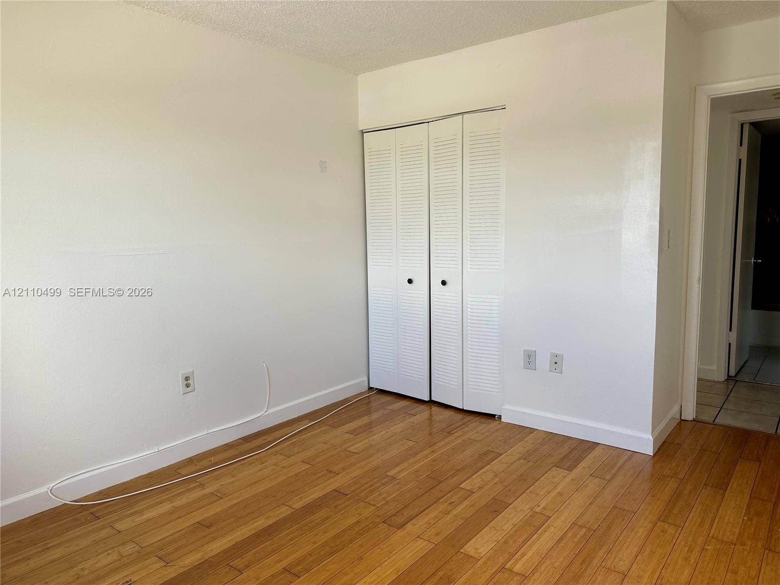 8145 NW 7th Street, #308, Miami, Miami, FL 33126 Room featuring wood-finish flooring, white walls, and a closet with white louvered bifold doors