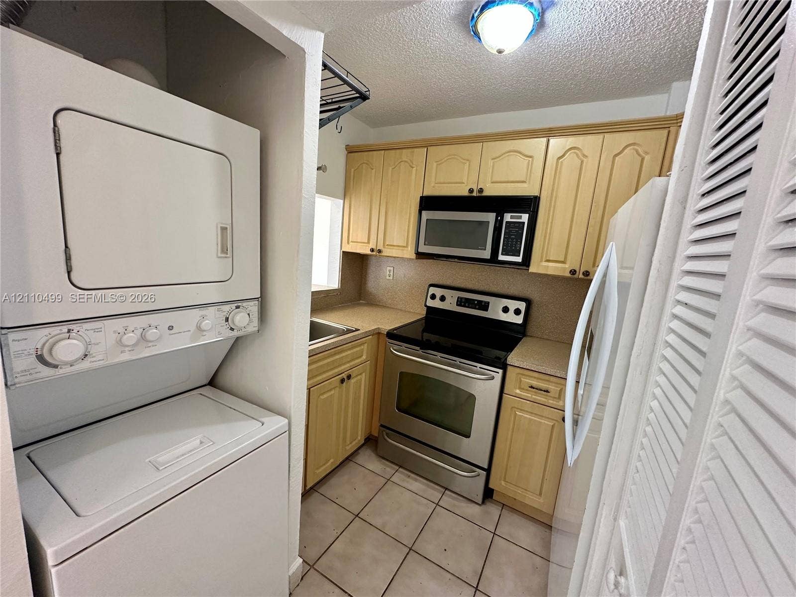 8145 NW 7th Street, #308, Miami, Miami, FL 33126 Kitchen featuring wood cabinetry, stainless steel appliances, a built-in microwave, tiled flooring, and an integrated laundry closet