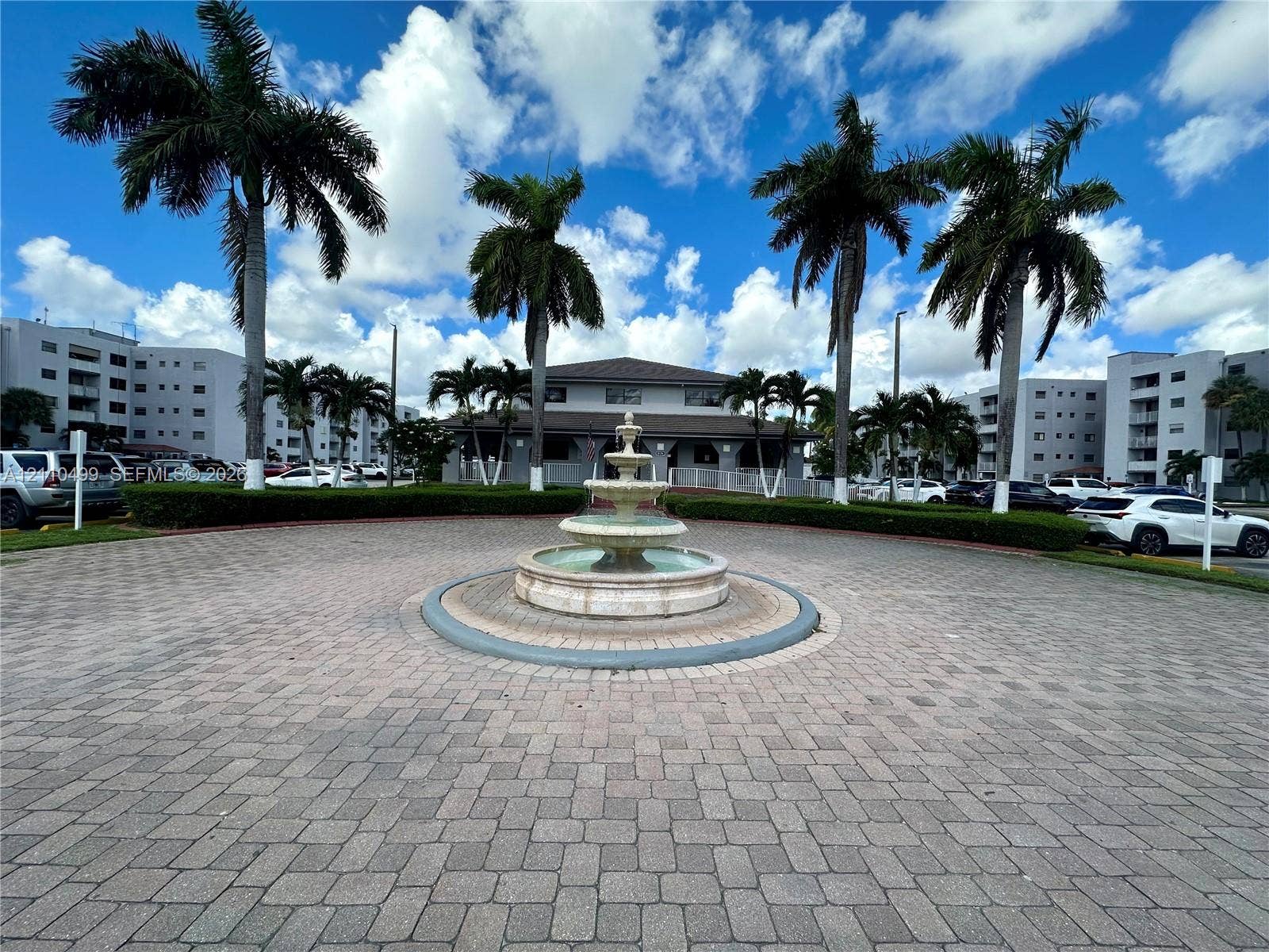 8145 NW 7th Street, #308, Miami, Miami, FL 33126 Circular paver driveway featuring a tiered stone fountain, mature palm trees, and manicured hedges
