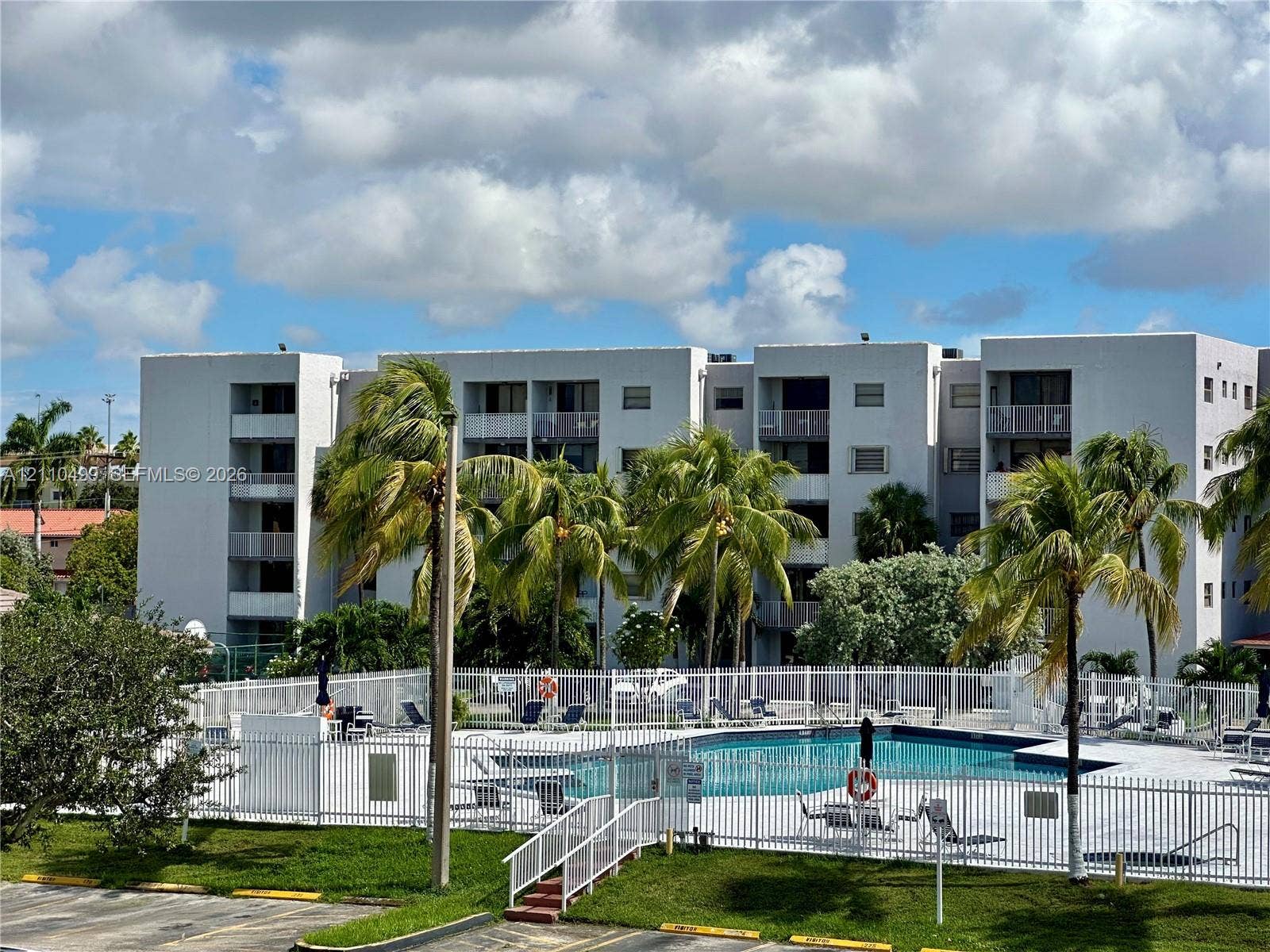 8145 NW 7th Street, #308, Miami, Miami, FL 33126 Multi-story residential building featuring private balconies, swimming pool with perimeter fencing, and mature palm trees