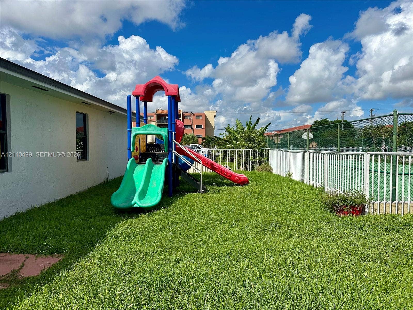 8145 NW 7th Street, #308, Miami, Miami, FL 33126 Outdoor space featuring a grass lawn, metal perimeter fencing, and a hard-surfaced sport court