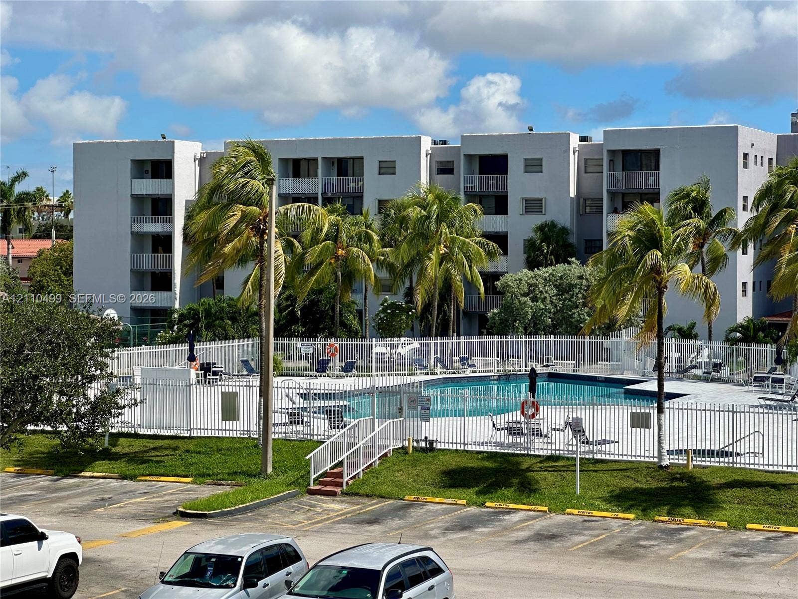 8145 NW 7th Street, #308, Miami, Miami, FL 33126 Multi-story residential building featuring private balconies, an enclosed swimming pool, metal perimeter fencing, and mature palm trees
