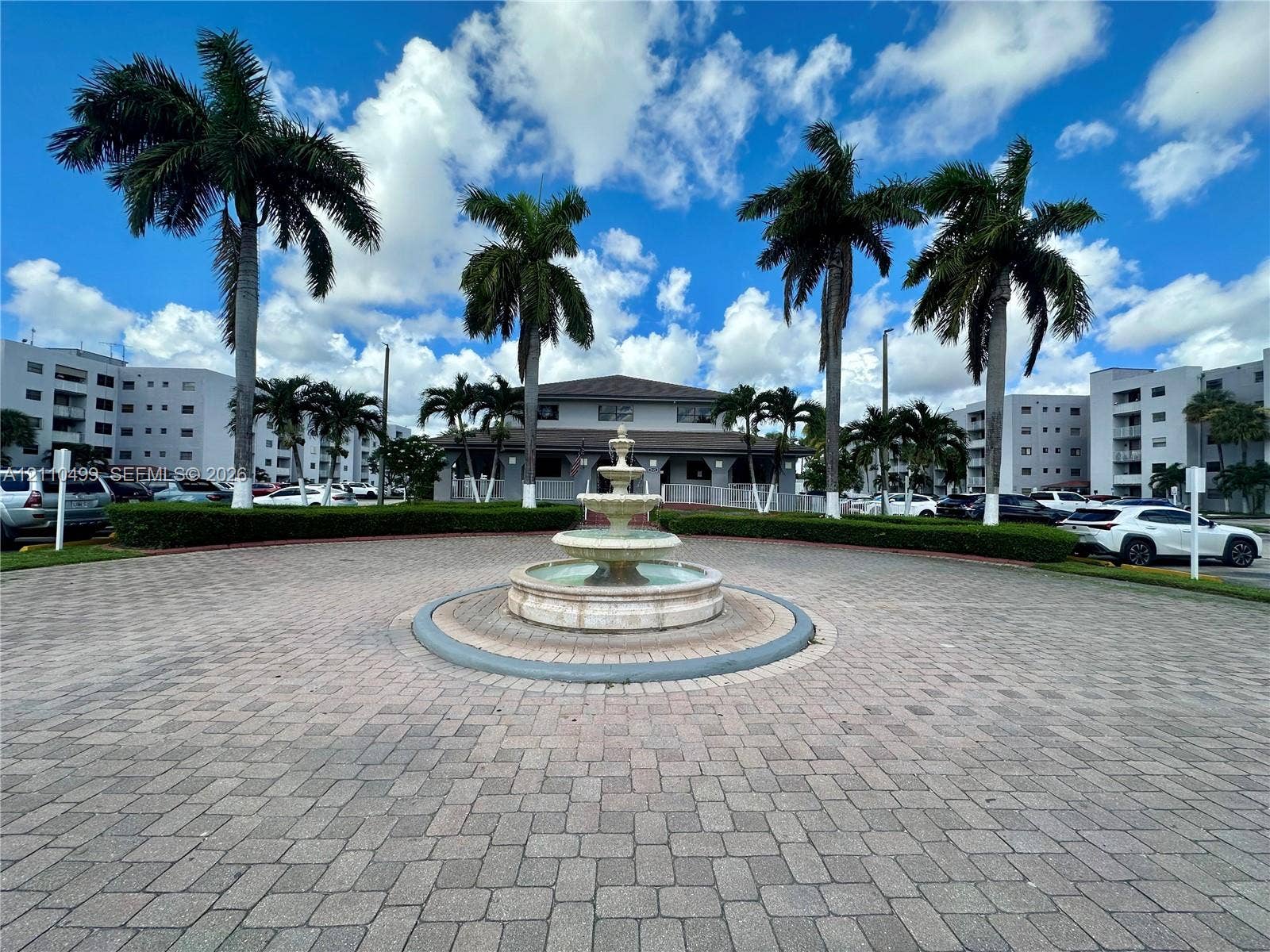 8145 NW 7th Street, #308, Miami, Miami, FL 33126 Circular paved motor court featuring a multi-tiered stone fountain, manicured hedges, and mature palm trees