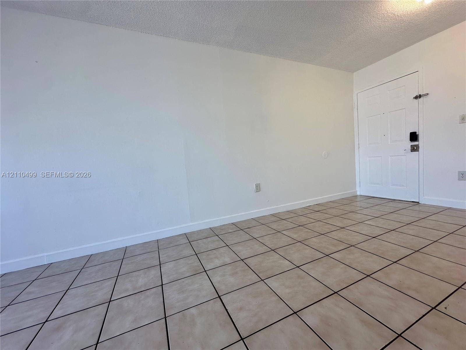 8145 NW 7th Street, #308, Miami, Miami, FL 33126 Neutral-toned interior space featuring white walls, square ceramic floor tile, and a white six-panel entry door with a digital deadbolt