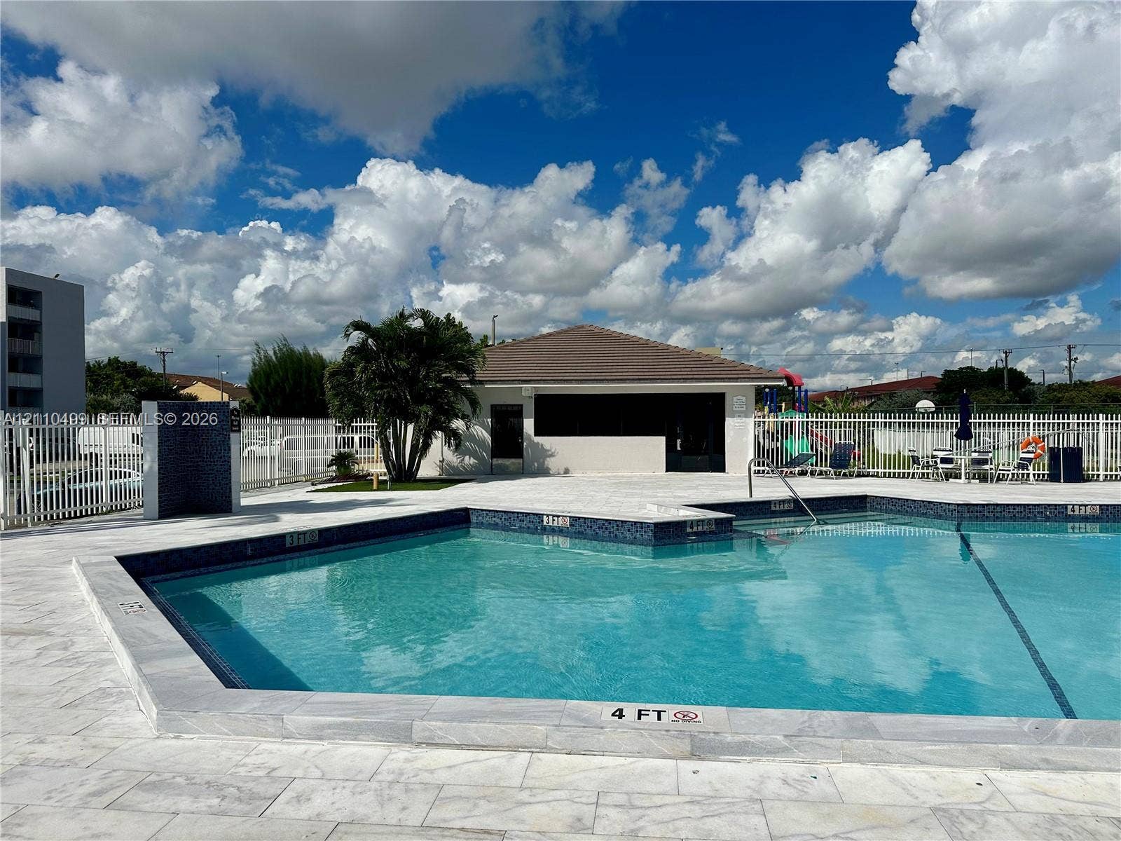 8145 NW 7th Street, #308, Miami, Miami, FL 33126 Swimming pool with stone-tiled decking, decorative tile waterline, and surrounding metal fencing