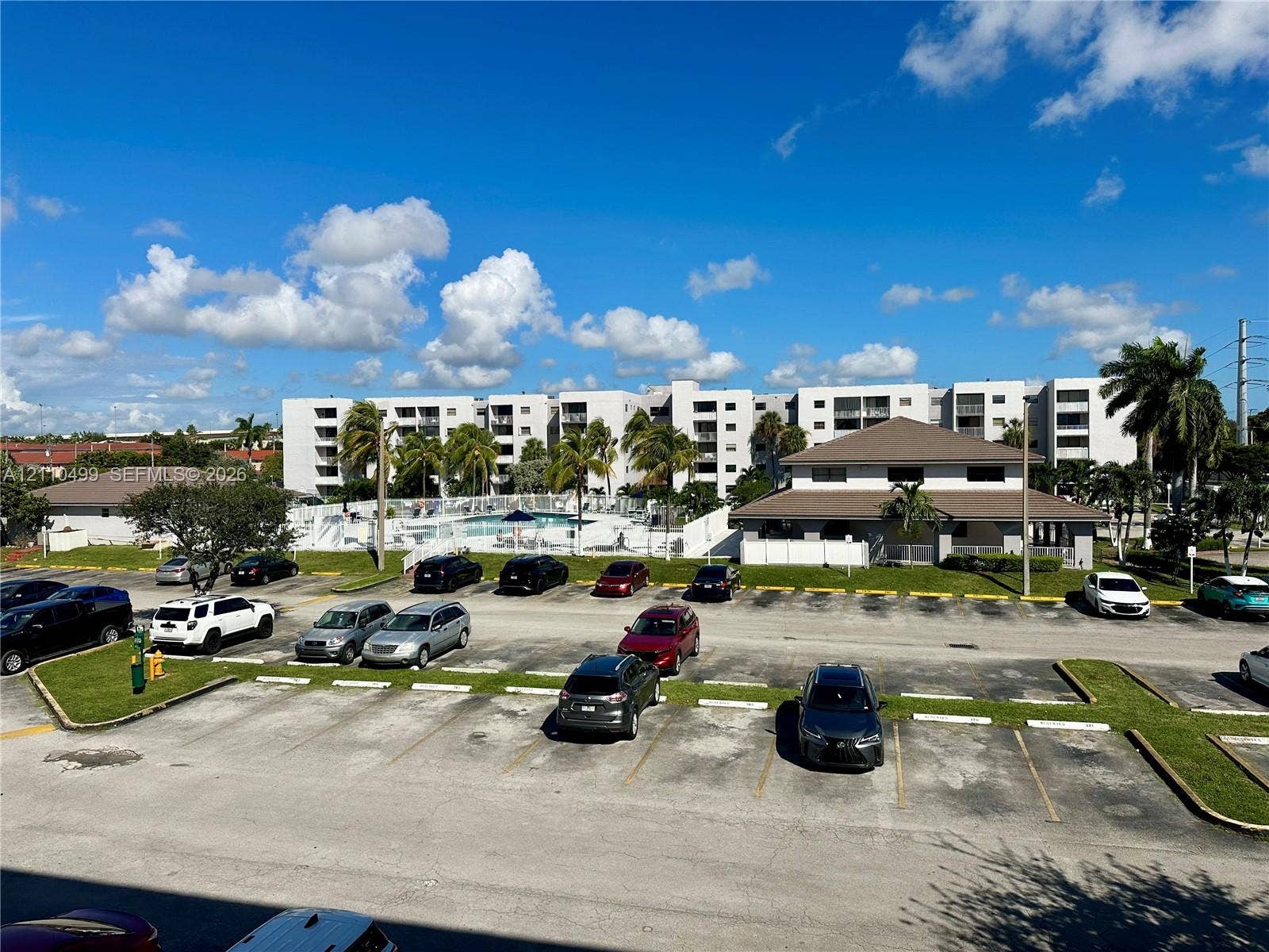 8145 NW 7th Street, #308, Miami, Miami, FL 33126 Multi-story residential complex featuring a swimming pool, mature palm trees, paved parking lot, and ground-level common area building