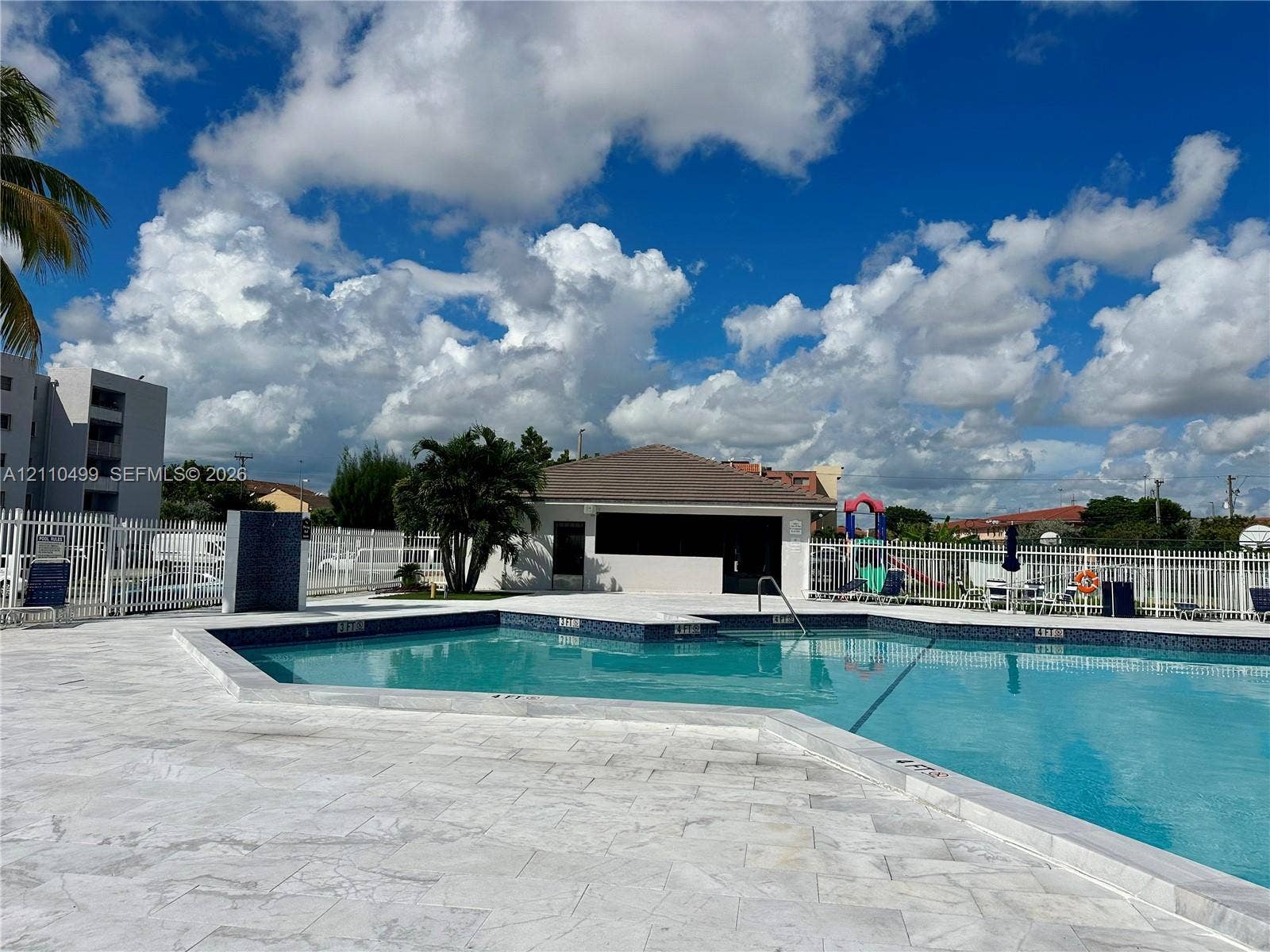 8145 NW 7th Street, #308, Miami, Miami, FL 33126 In-ground swimming pool with tile trim, expansive stone-paver pool deck, and enclosed perimeter fencing