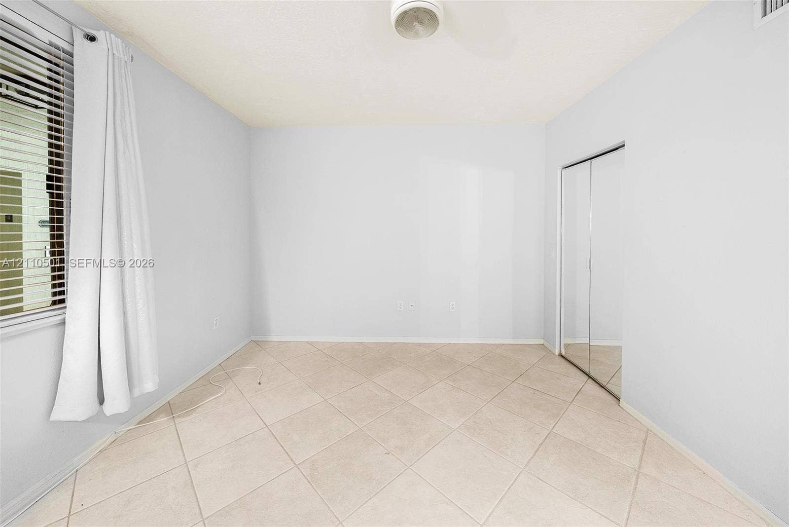 Neutral-toned room featuring ceramic tile flooring, sliding mirror-panel closet doors, and horizontal window blinds