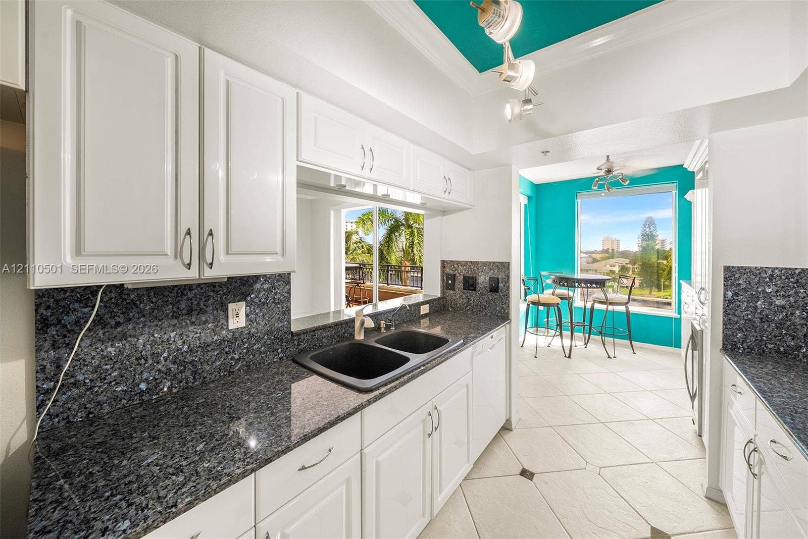 Kitchen featuring white cabinetry, dark stone countertops, dual basin undermount sink, tray ceiling with recessed lighting, and large picture windows