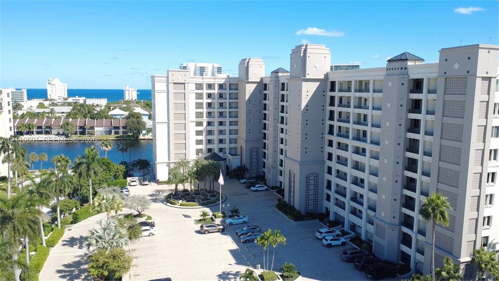 High-rise residential exterior featuring multi-story masonry construction, private balconies, paved surface parking, and waterfront grounds with mature palm trees