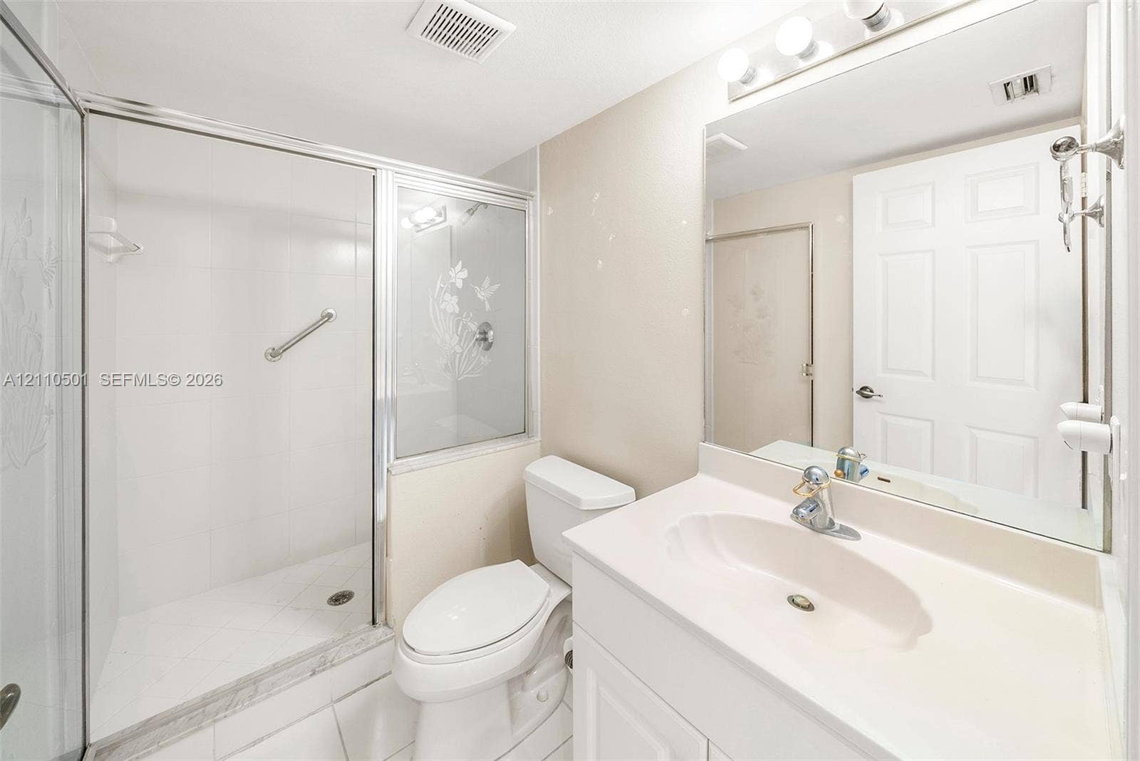 Bathroom featuring a glass-enclosed shower with etched detail, vanity with an integrated sink, polished chrome fixtures, and a large wall-mounted mirror