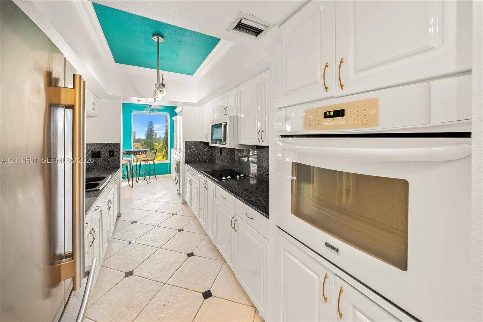 Kitchen featuring white cabinetry, dark stone-finish countertops, stainless steel appliances, built-in double oven, and tile flooring with decorative inserts