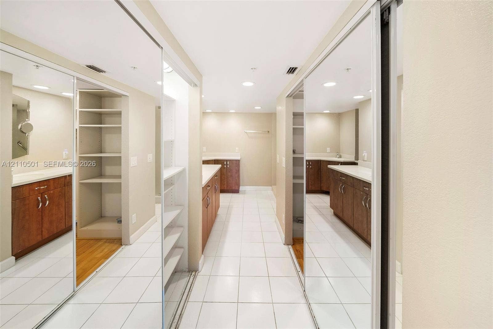 Walk-in dressing area featuring floor-to-ceiling mirrored sliding closet doors, built-in shelving, wood-finish cabinetry, neutral countertops, and white tile flooring