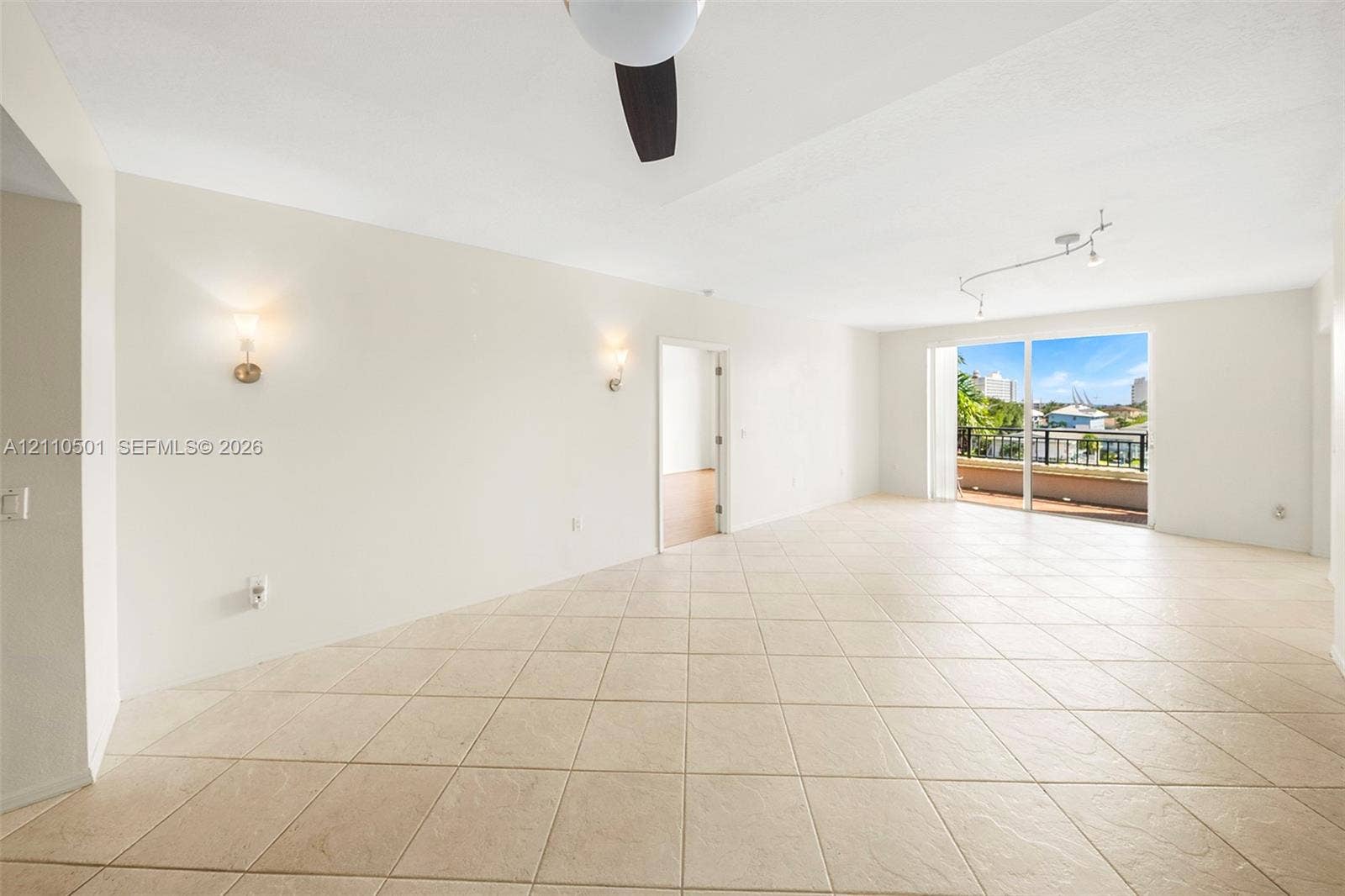 Large-format tile flooring, wall-mounted light fixtures, ceiling fan with light kit, adjustable track lighting, and sliding glass doors with access to an exterior terrace