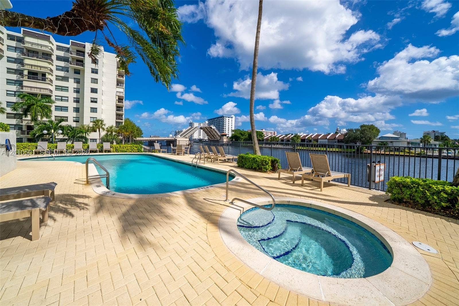 Waterfront pool area featuring a curved swimming pool, integrated spa, paver patio, and metal perimeter fencing
