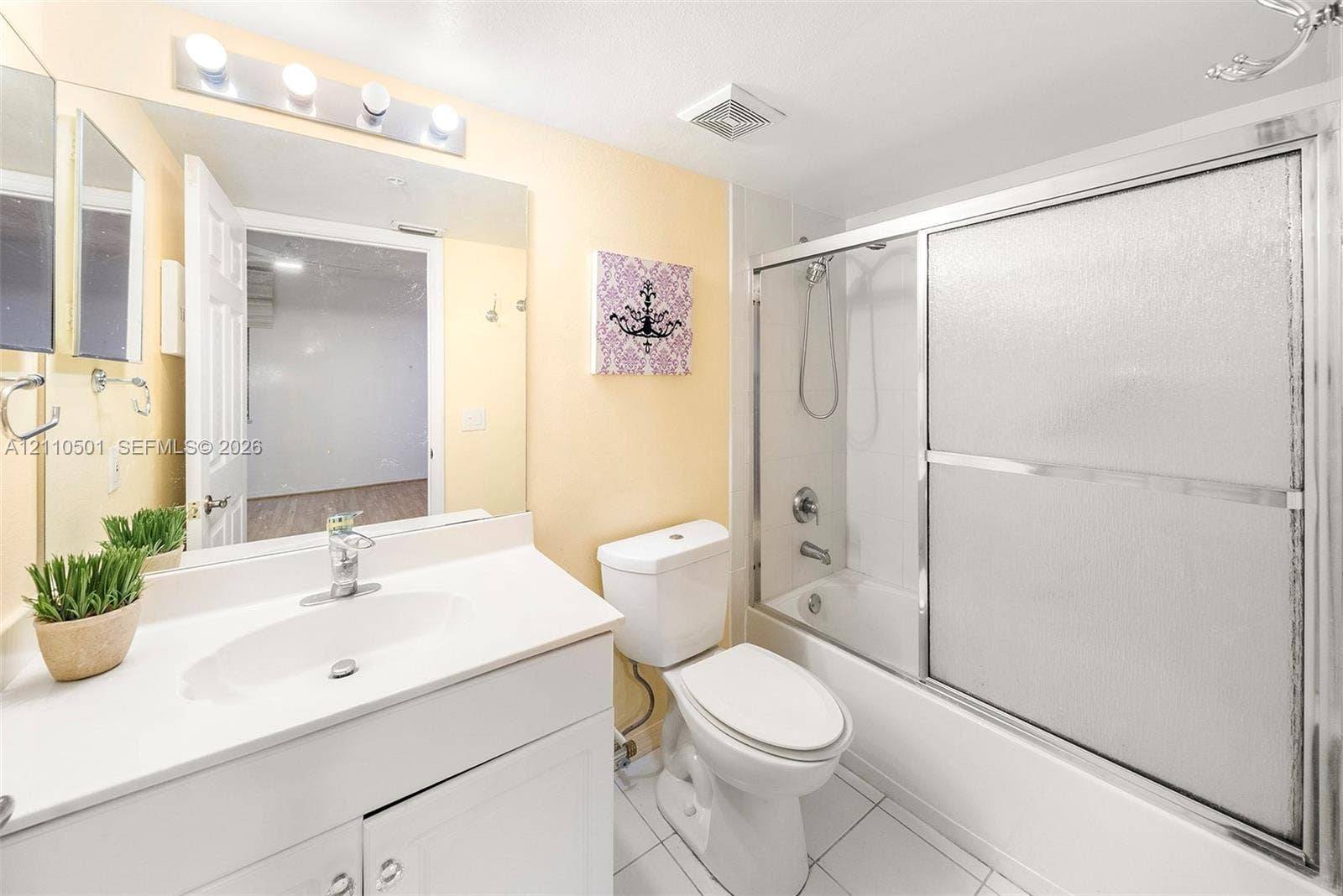 Bathroom featuring a white vanity with an integrated sink, a large wall-mounted mirror, a four-light fixture, and a tub-shower combination with sliding glass doors