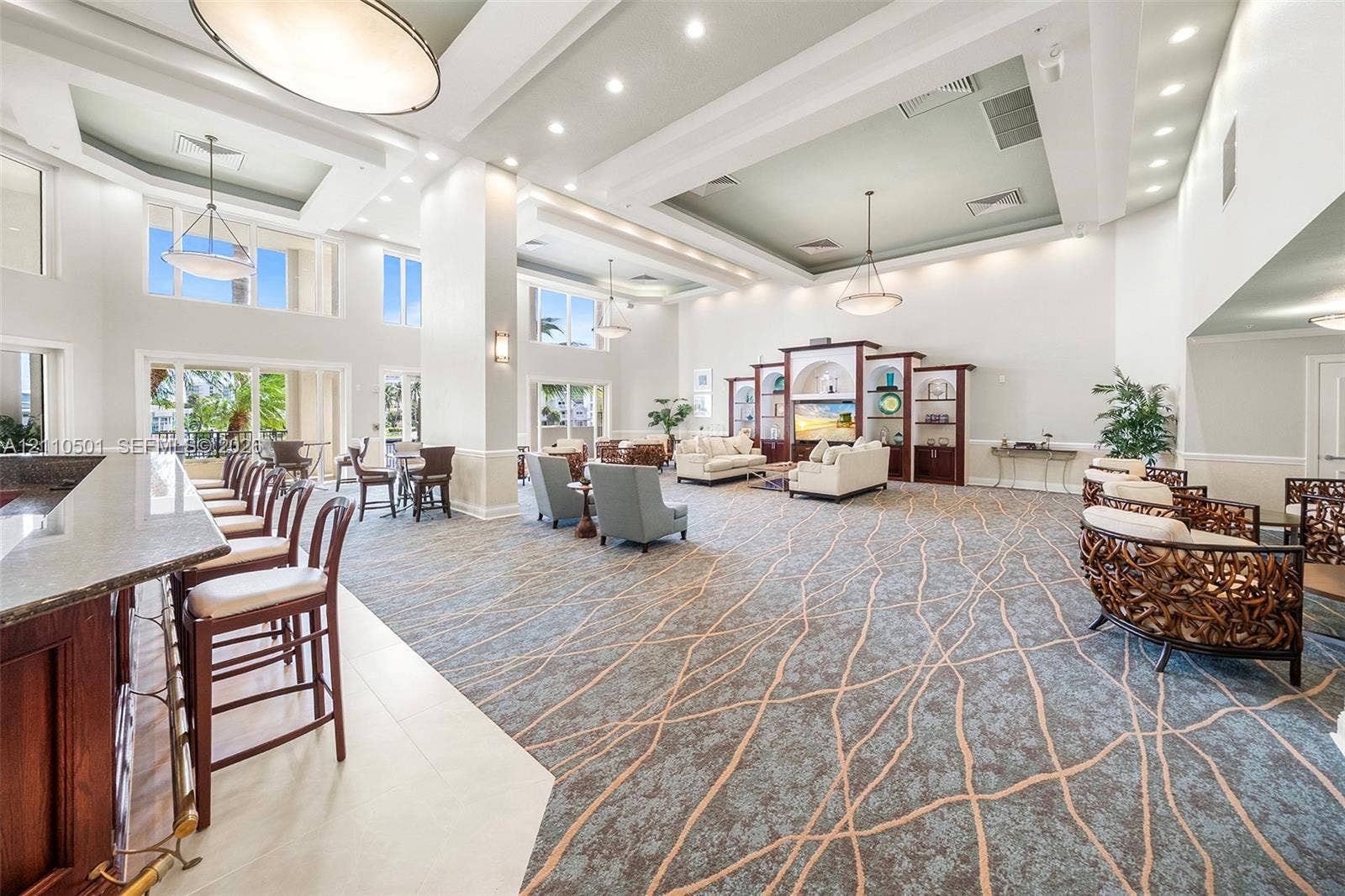 Expansive communal space featuring coffered ceilings, recessed lighting, integrated wooden shelving, a stone-topped bar with built-in seating, and tile and carpet flooring