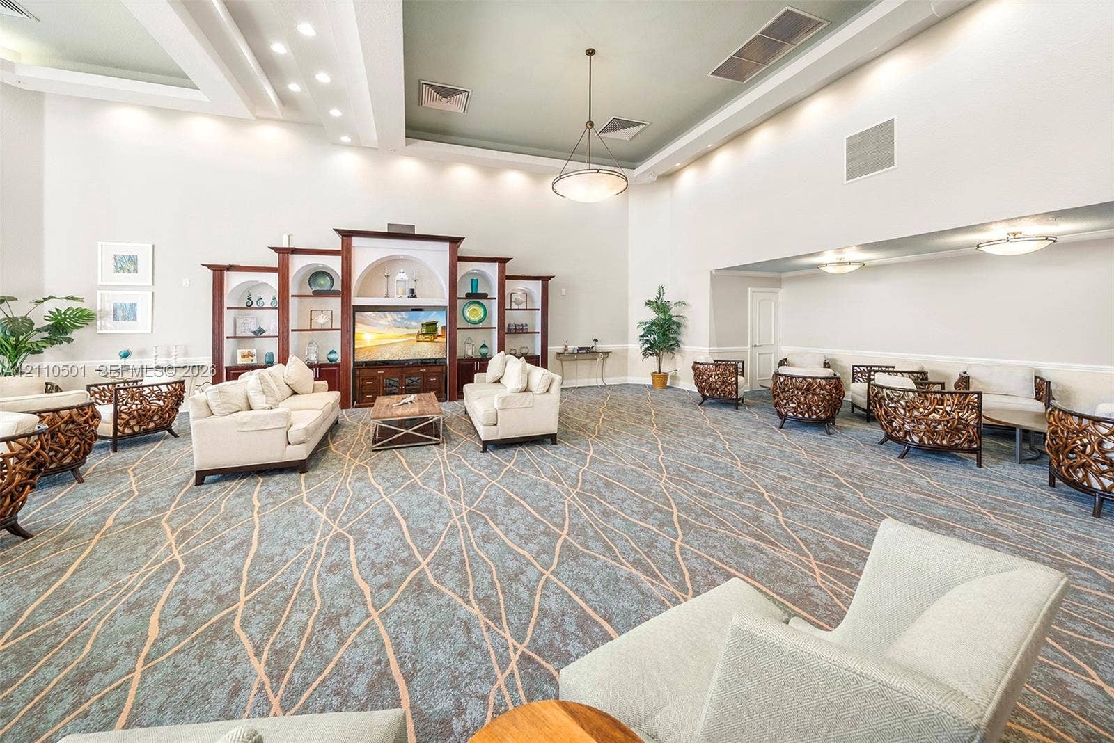 Expansive room featuring high tray ceilings, built-in recessed cabinetry with arched shelving, integrated cove lighting, and patterned carpeting
